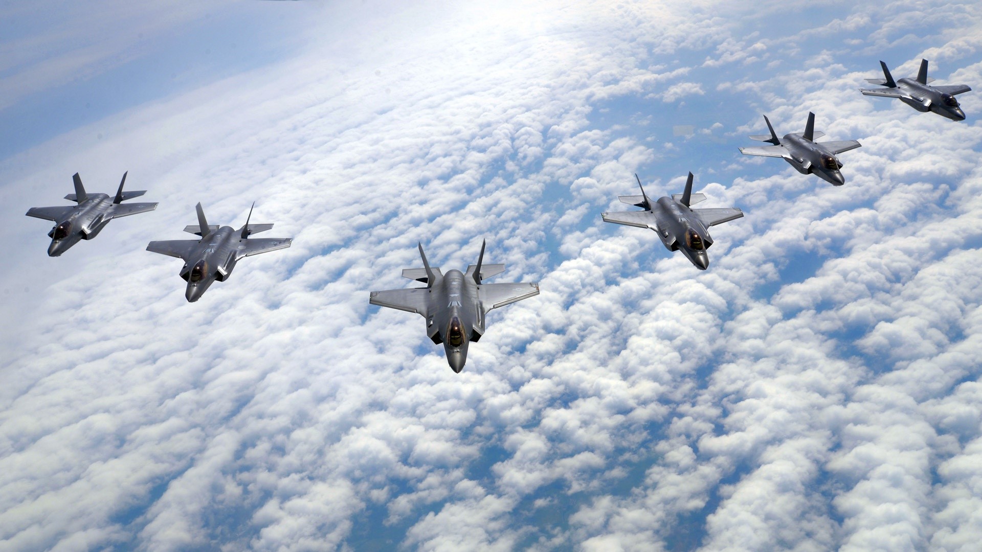 Formation of F-35A Lightning II military aircraft flying above clouds HD Wallpaper