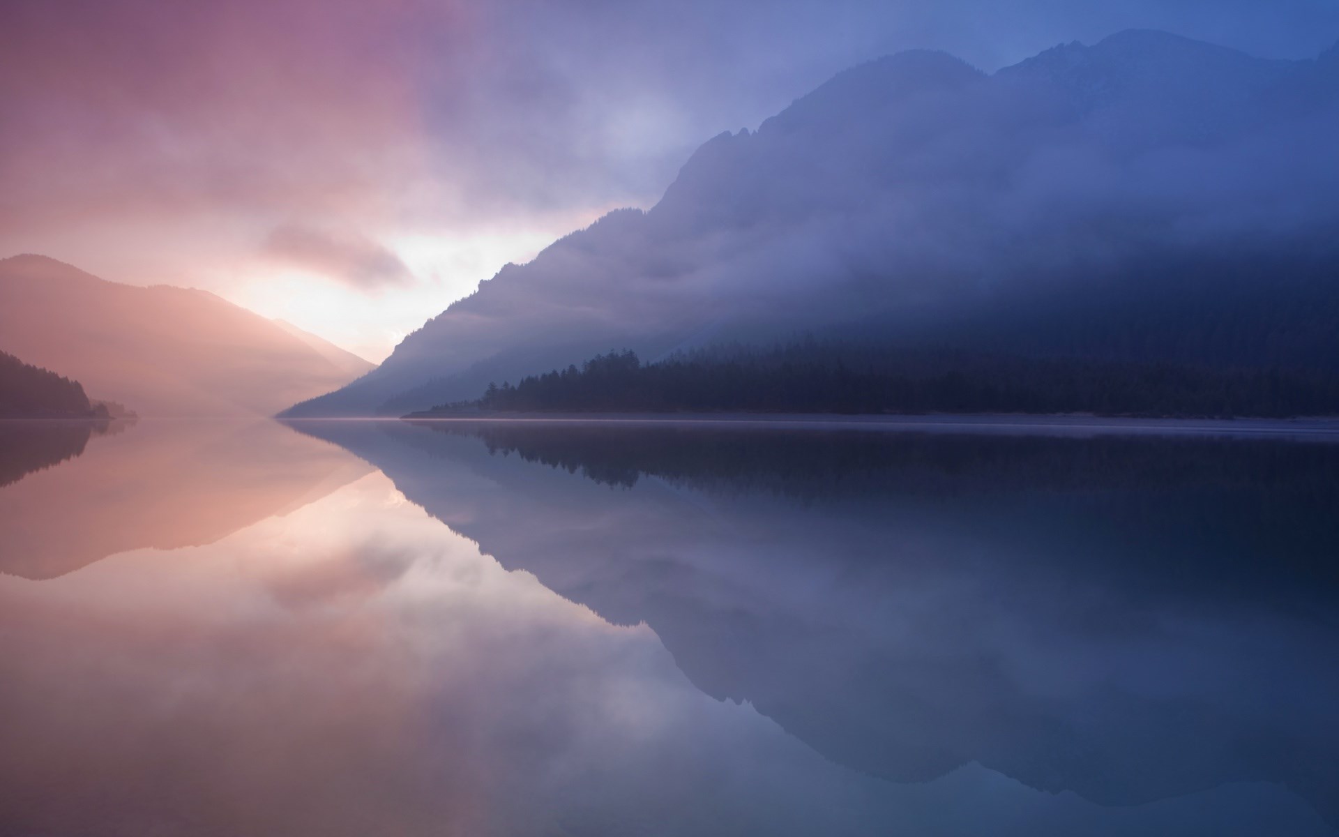 Misty mountains reflected in a calm lake at sunrise HD Wallpaper