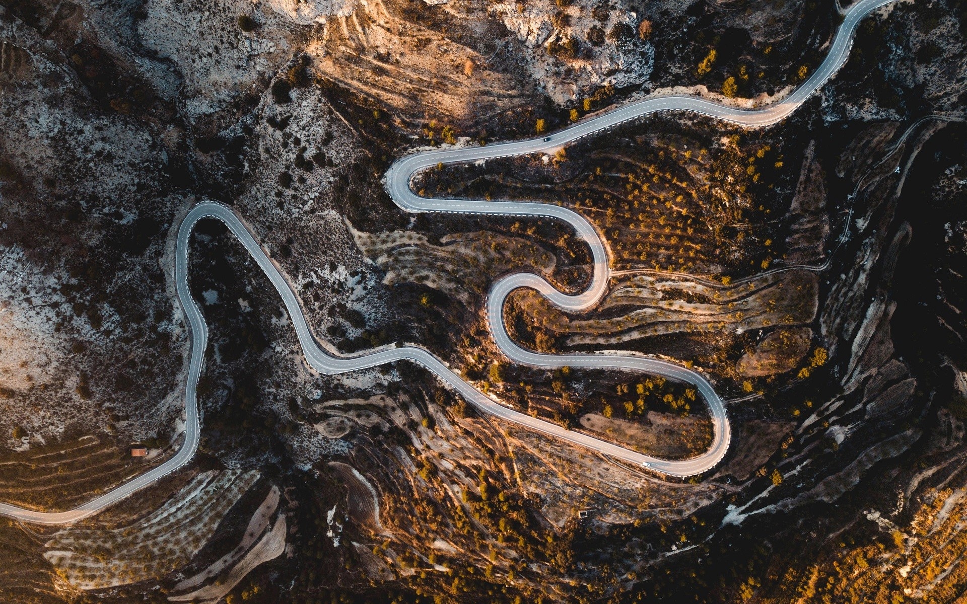 Aerial view of a winding mountain road with hairpin turns HD Wallpaper