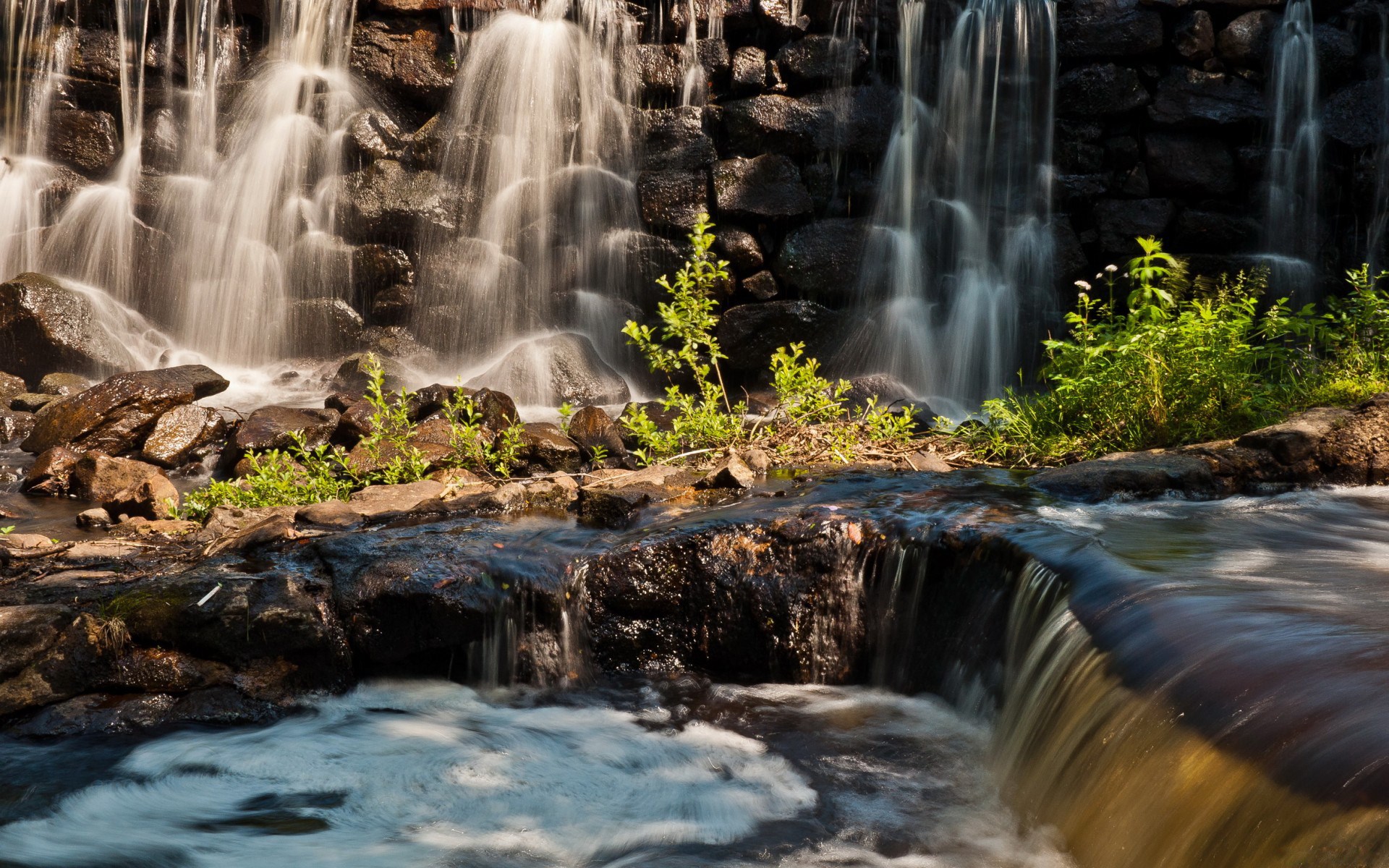 Waterfall cascading over dark rocks with green plants HD Wallpaper