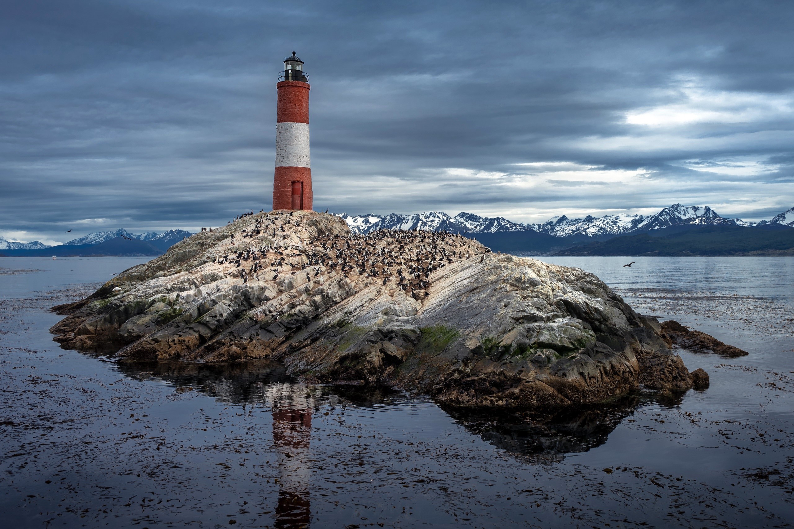 Lighthouse on a rocky island with snowy mountains HD Wallpaper