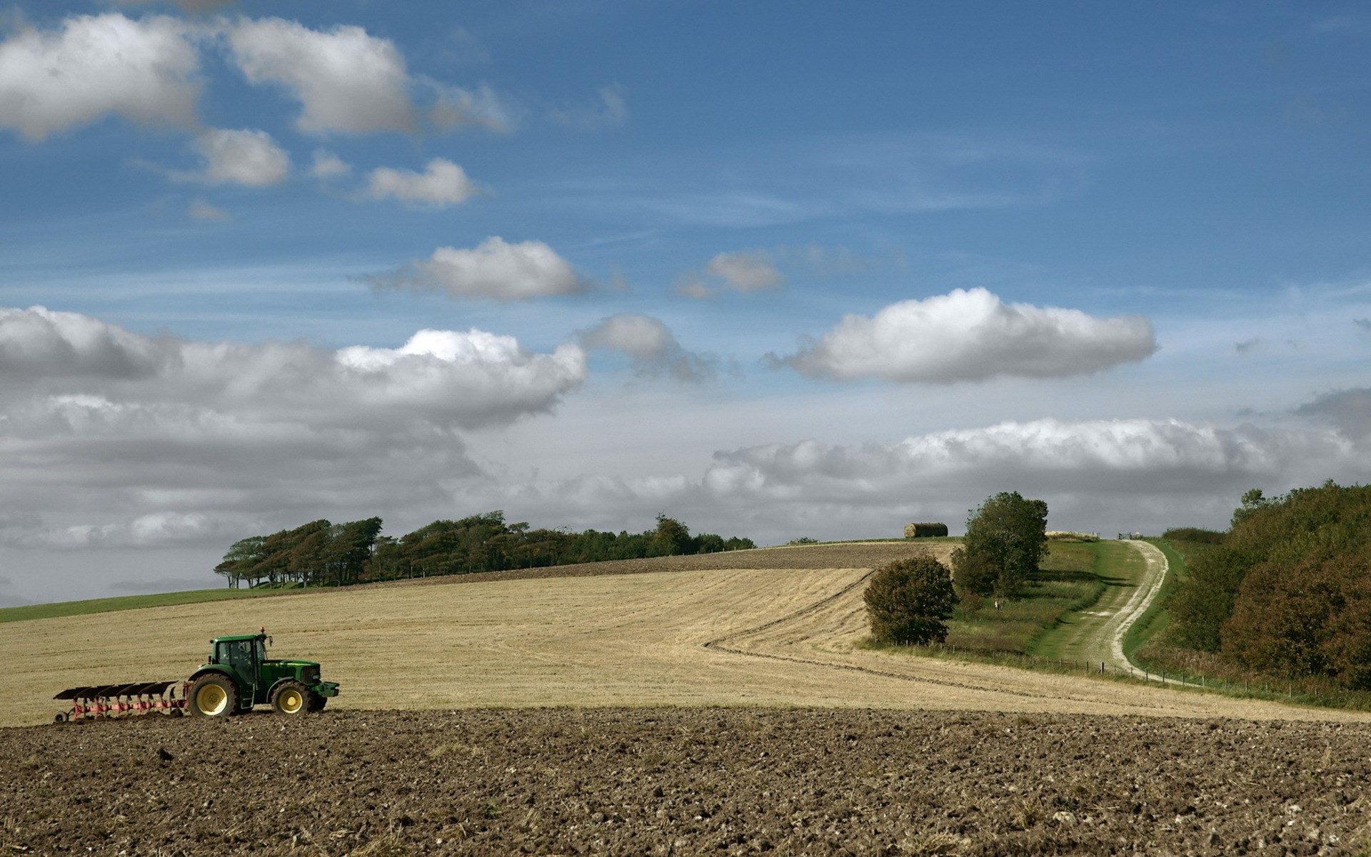 Tractor plowing a field under a cloudy sky HD Wallpaper