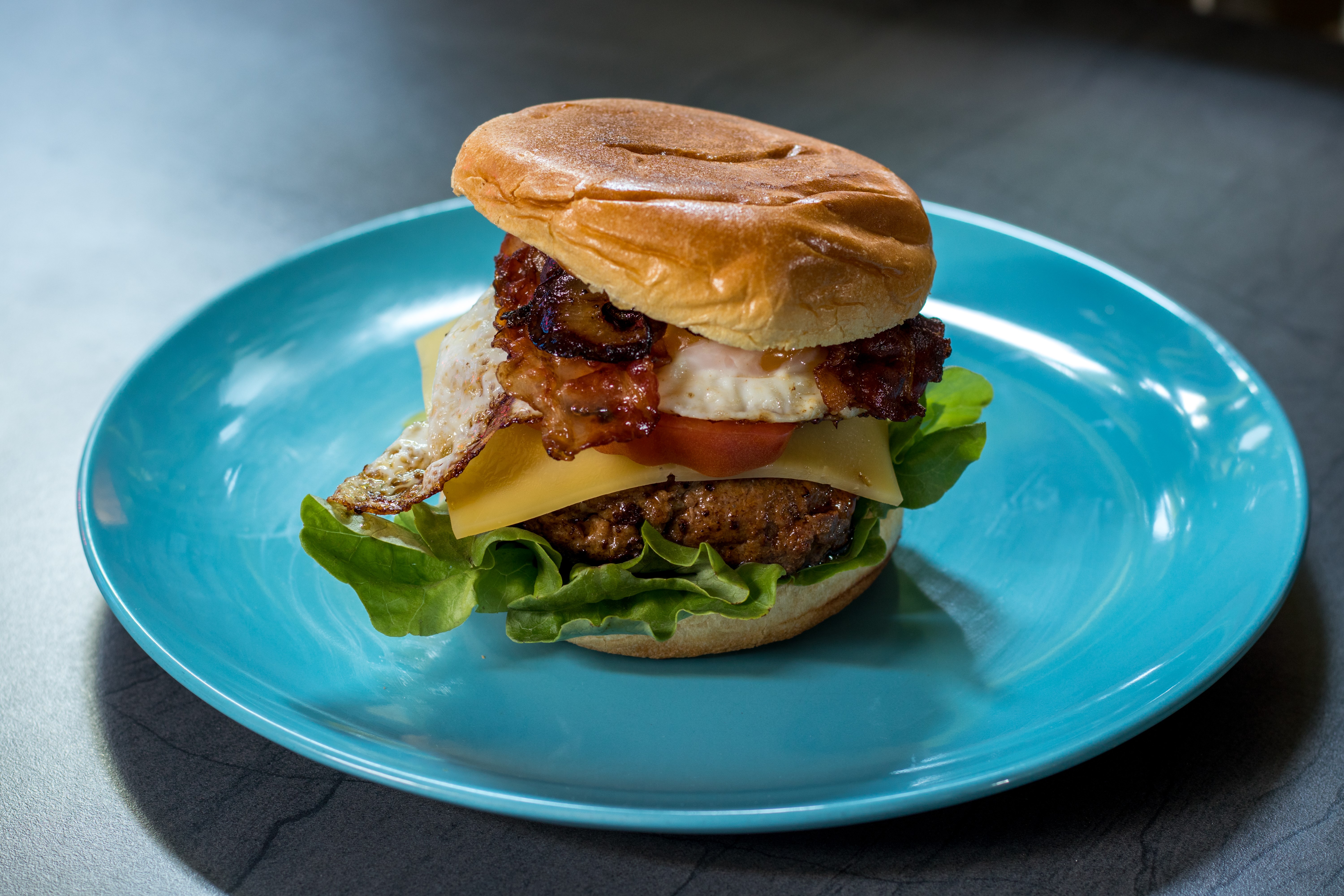 Burger with bacon, egg, cheese, and lettuce on a blue plate HD Wallpaper