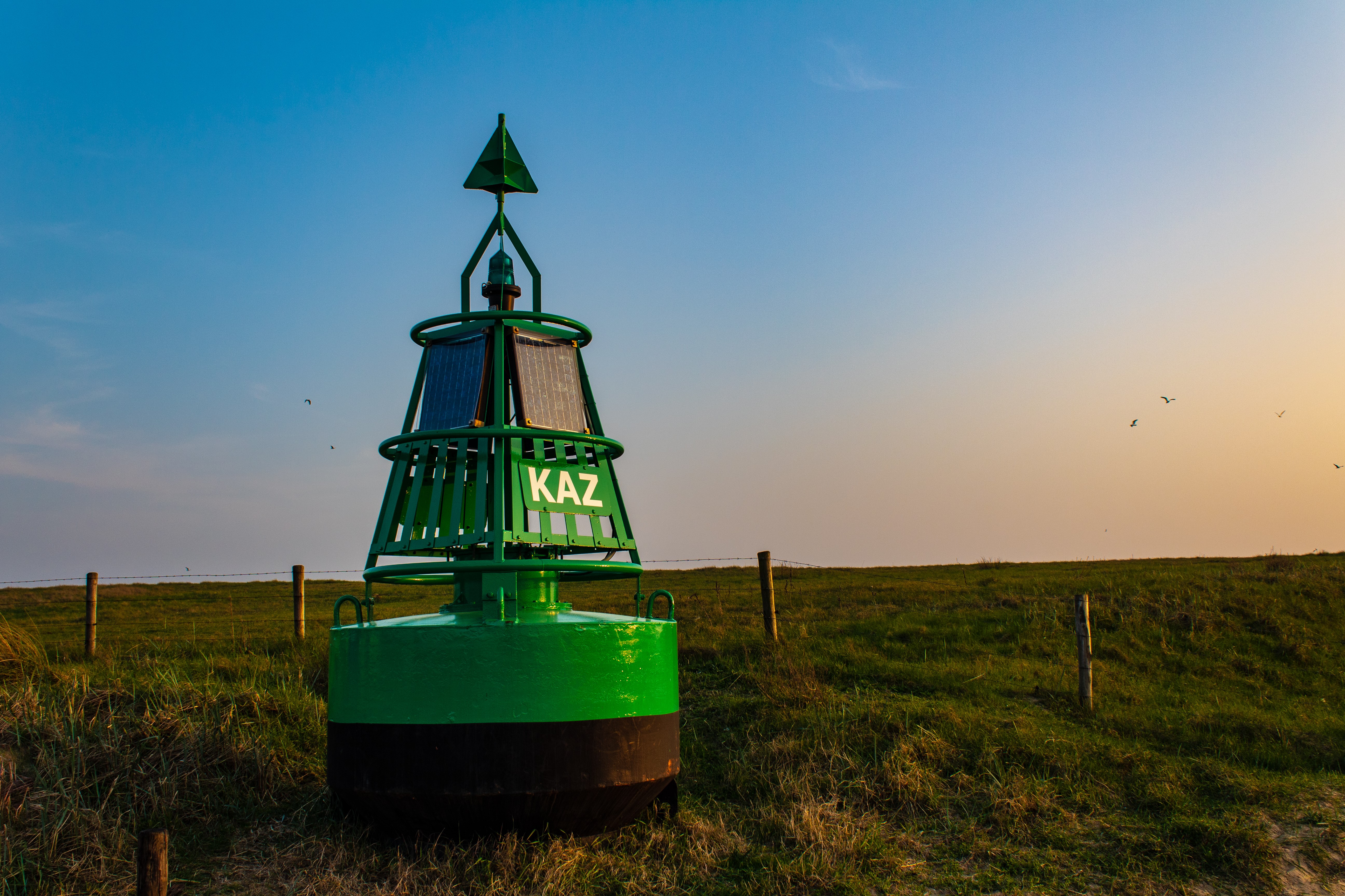 Green buoy with KAZ sign on grassy dune HD Wallpaper