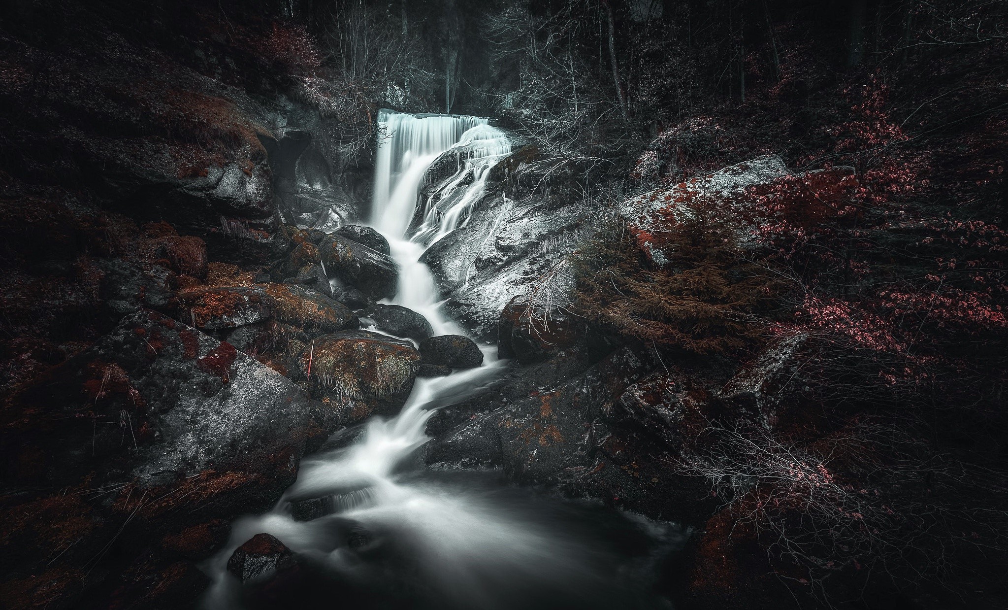 Waterfall cascading over mossy rocks in a dark forest HD Wallpaper
