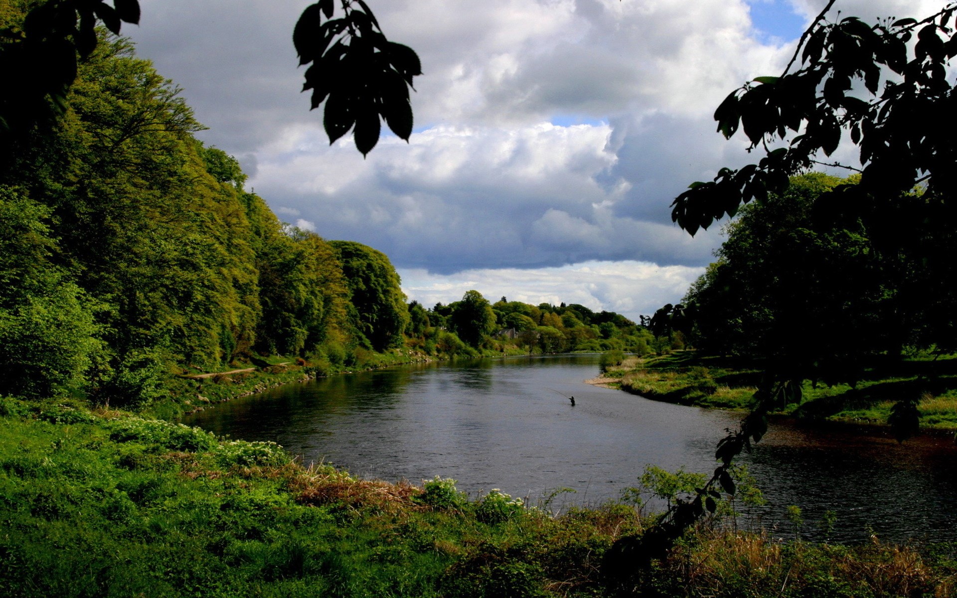 River flowing through a green landscape with trees and clouds HD Wallpaper