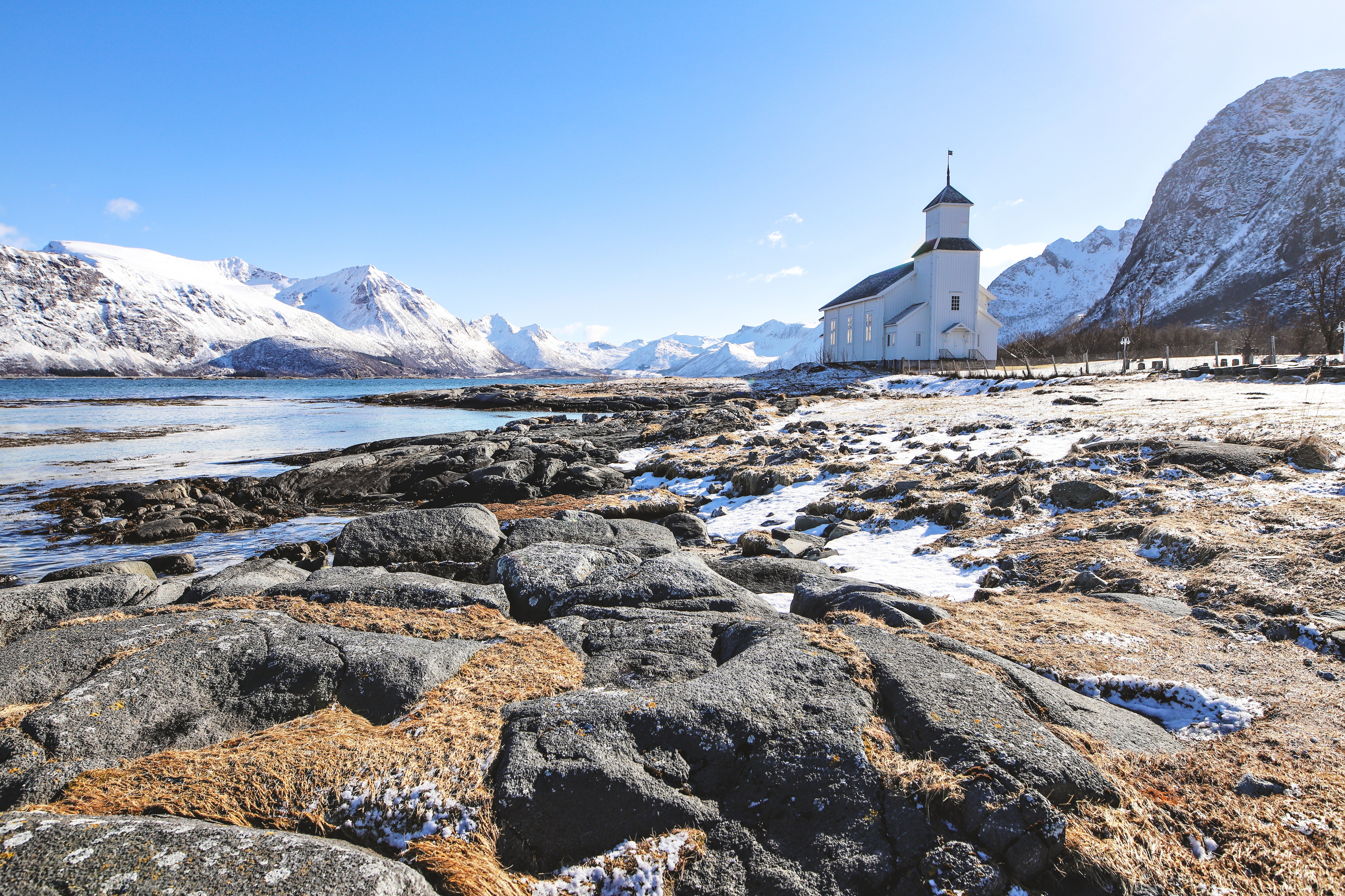 White church on a rocky beach with snow-capped mountains in Norway HD Wallpaper