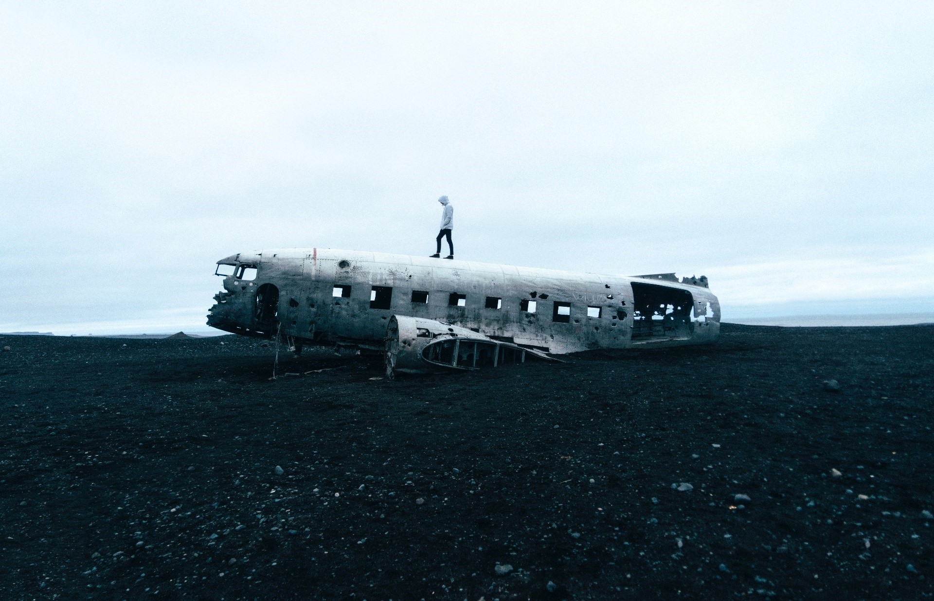 Person standing on a plane wreck on a black sand beach HD Wallpaper