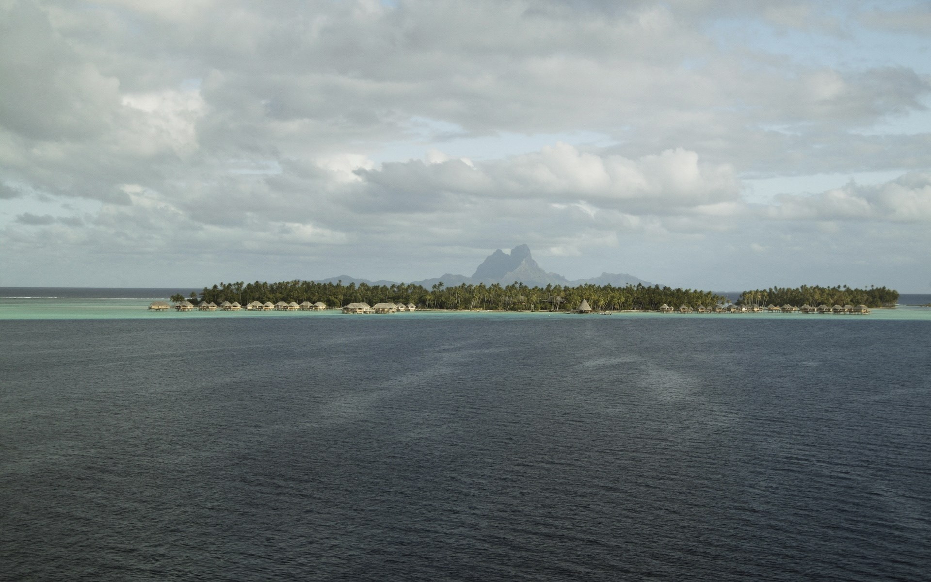 Overwater bungalows on a tropical island with mountains in the background HD Wallpaper