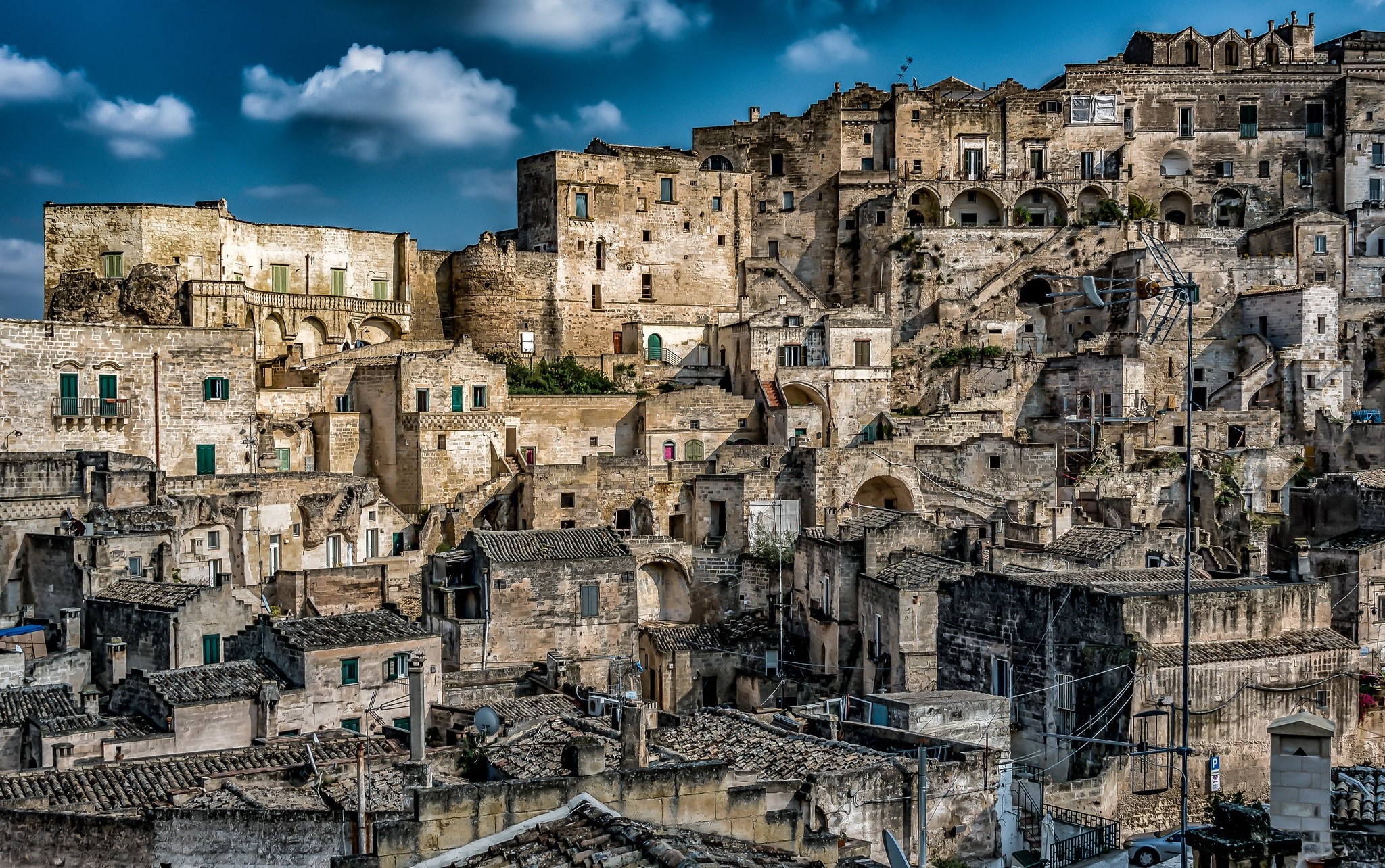 Ancient stone buildings on a hillside under a cloudy sky HD Wallpaper