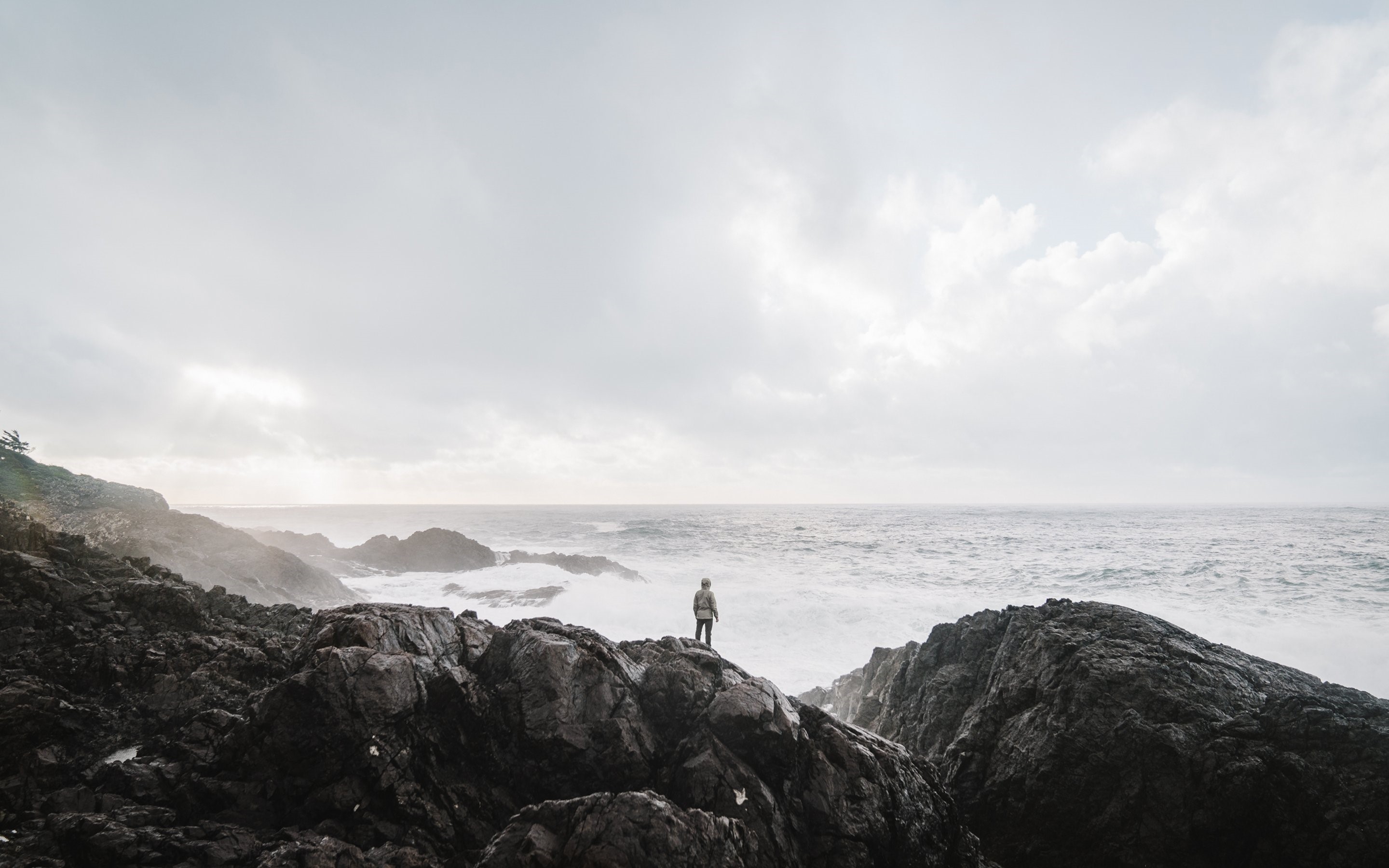 Person standing on rocks overlooking the sea HD Wallpaper