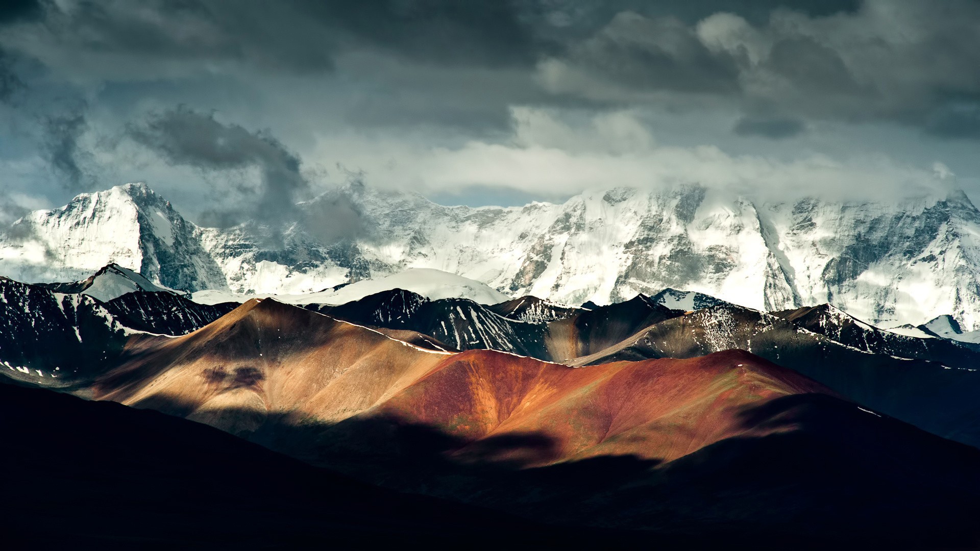 Snow-capped mountains under dramatic clouds HD Wallpaper