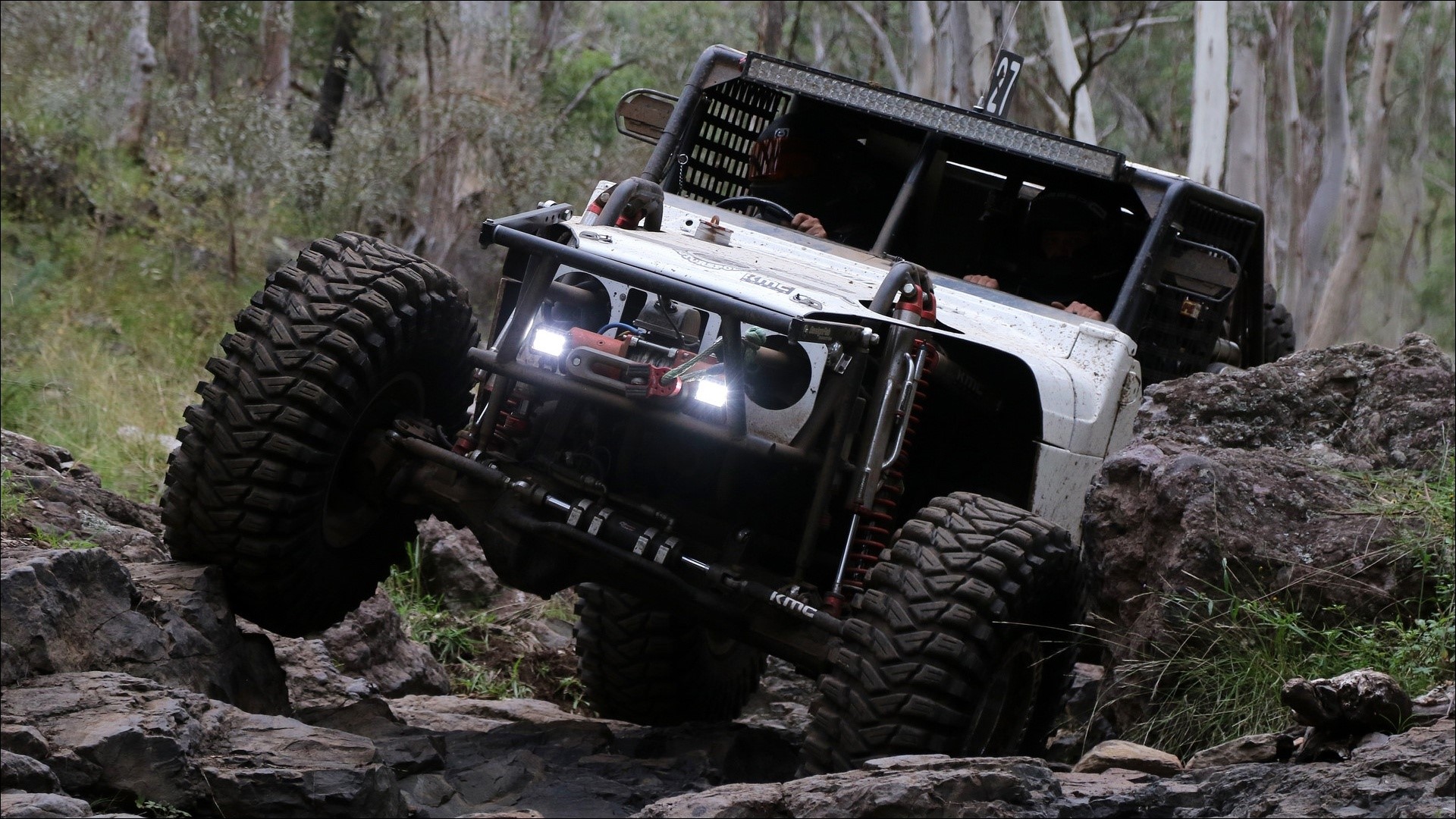 Off-road vehicle climbing rocks in a forest HD Wallpaper