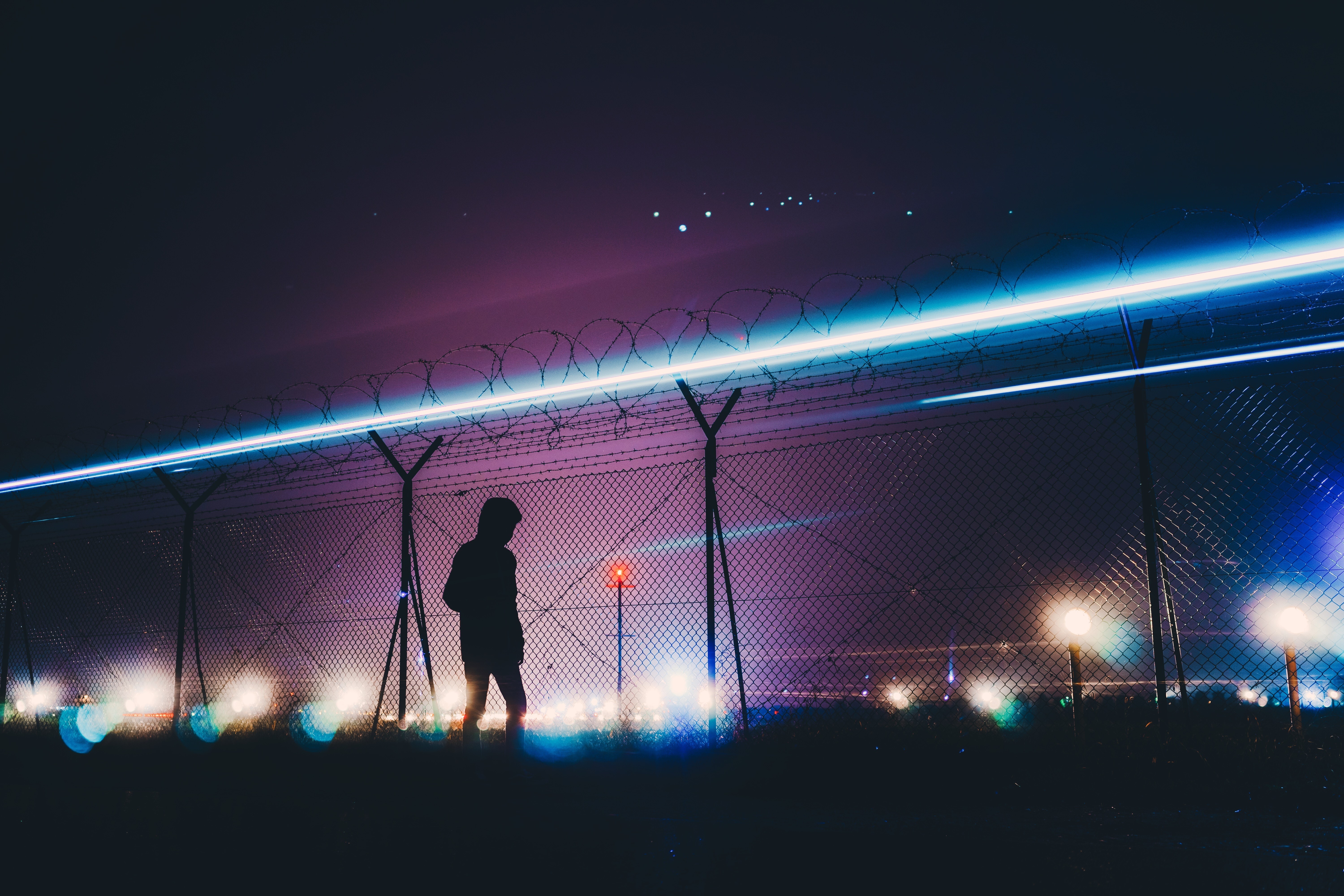 Silhouette by barbed wire fence with light trails at night HD Wallpaper