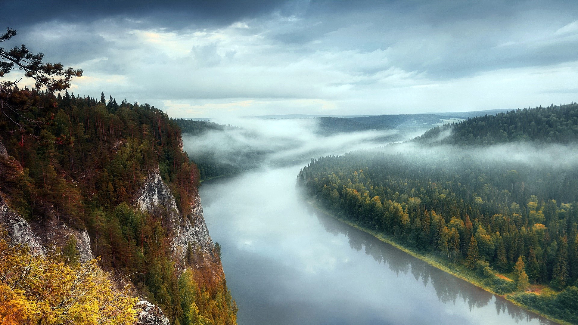 Misty river flowing through a dense forest with rocky cliffs HD Wallpaper