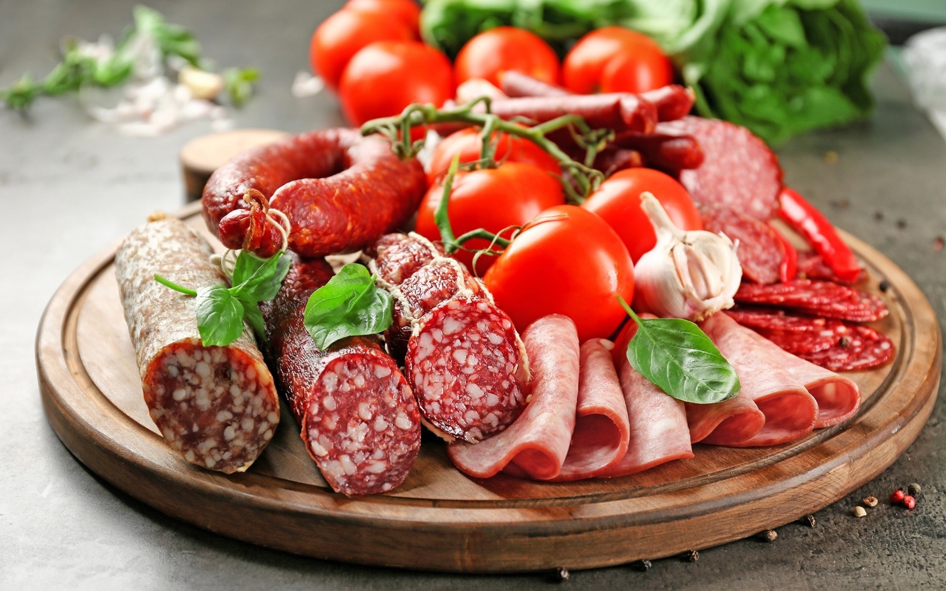 Assortment of cured meats, tomatoes, garlic, and basil on a wooden board HD Wallpaper