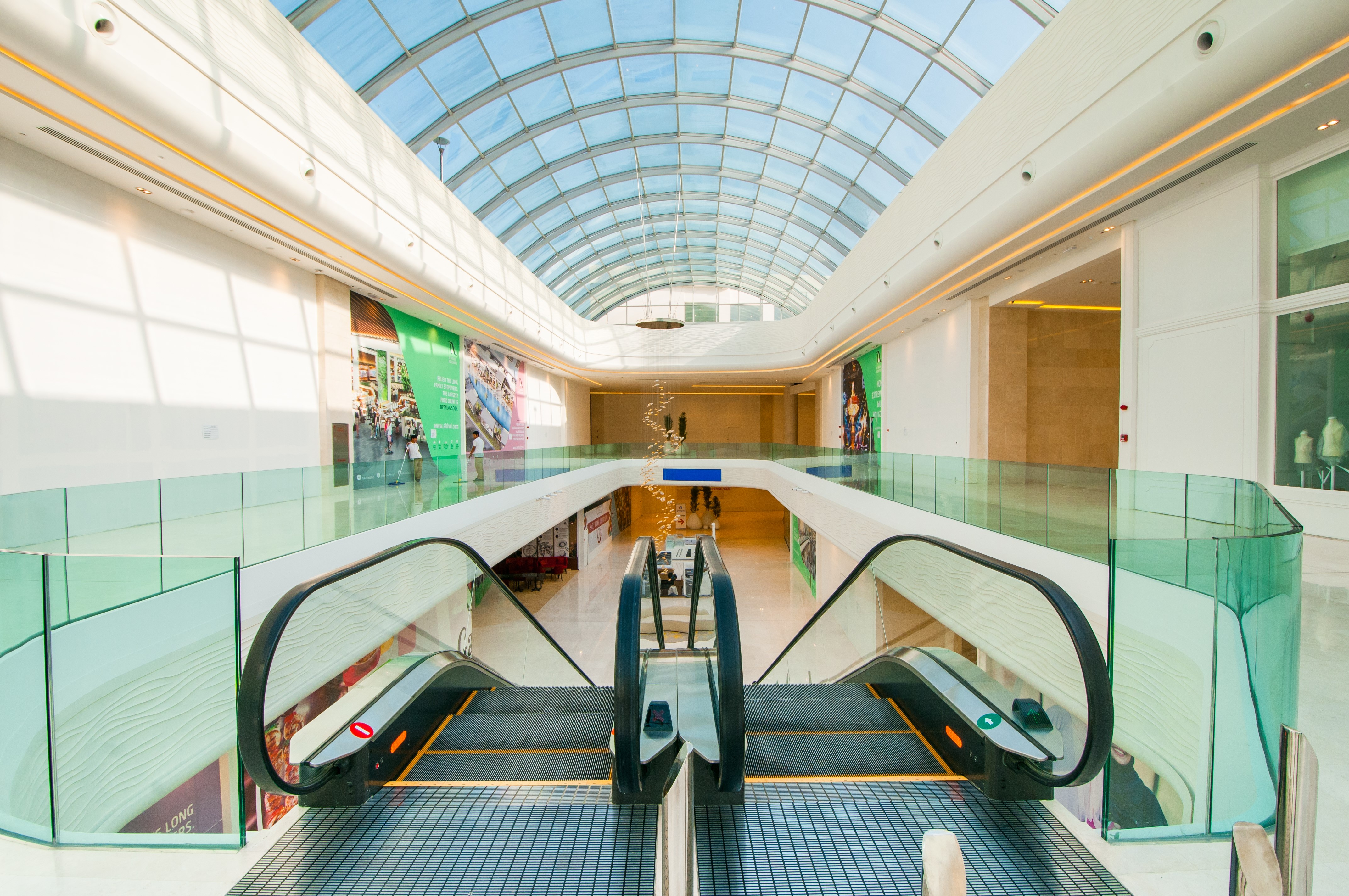Interior of a modern shopping mall with escalators and a glass roof HD Wallpaper