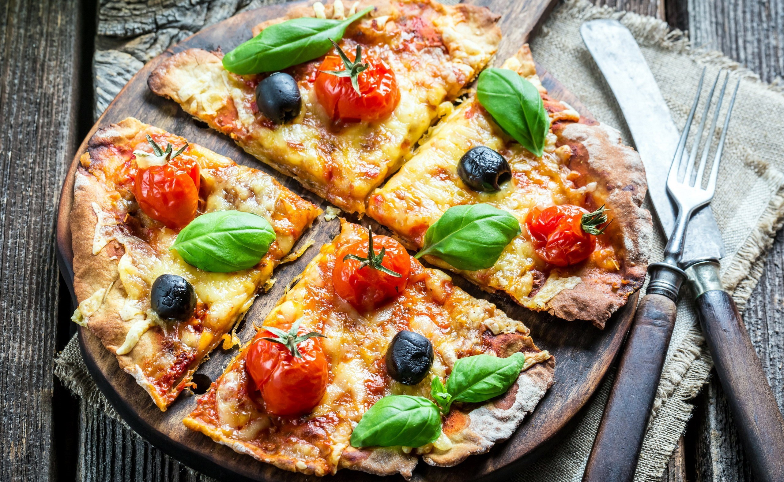 Pizza with tomatoes, olives, and basil on a wooden board HD Wallpaper