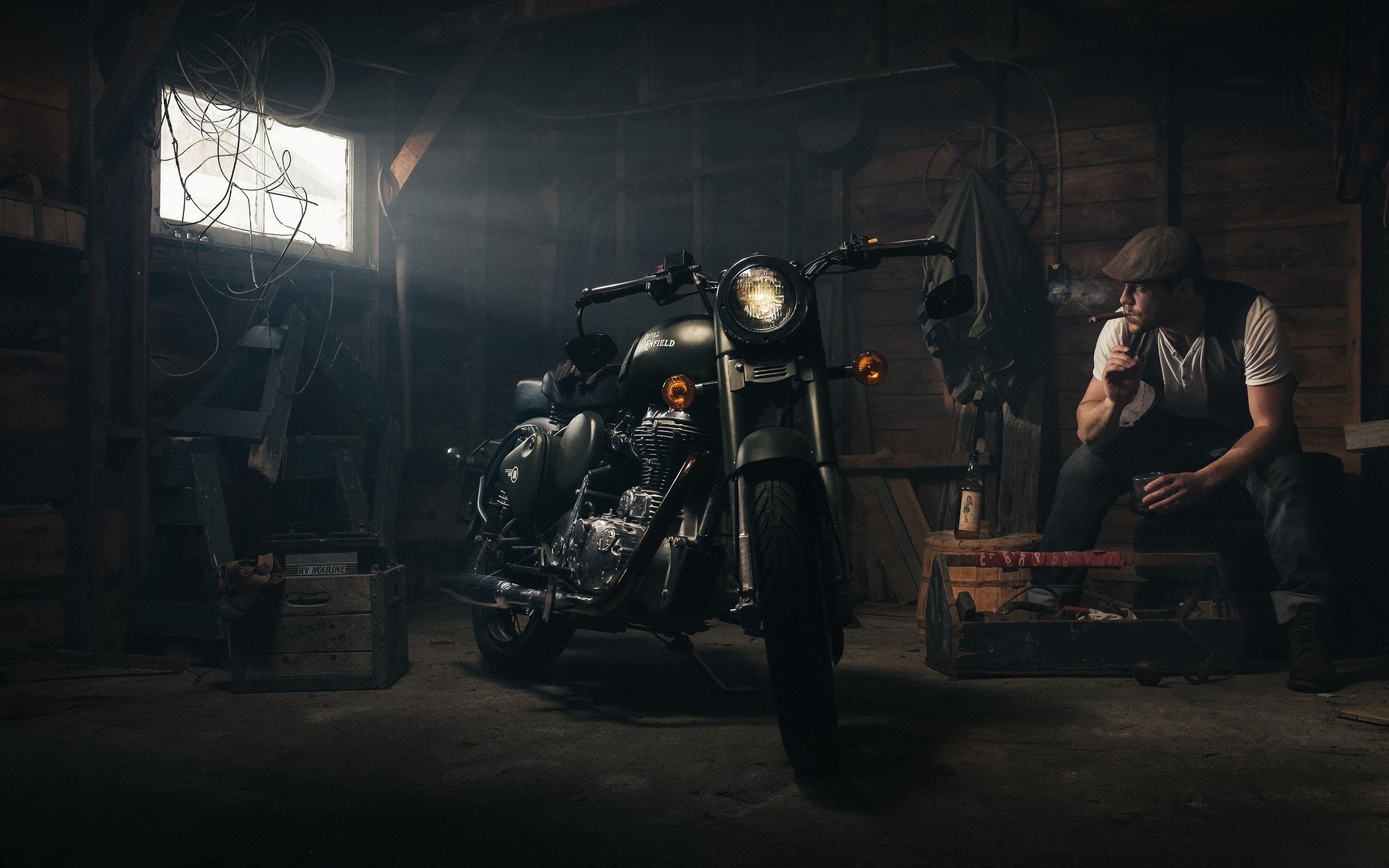 Man smoking cigarette next to motorcycle in garage HD Wallpaper