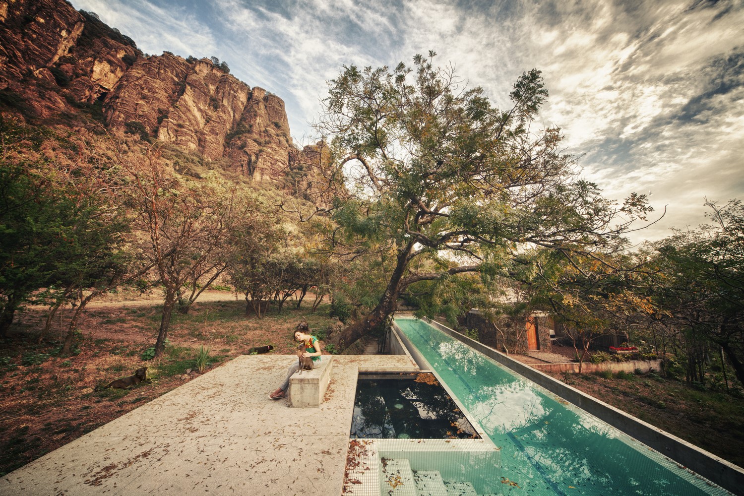 Woman sitting by a long swimming pool in a rocky landscape HD Wallpaper