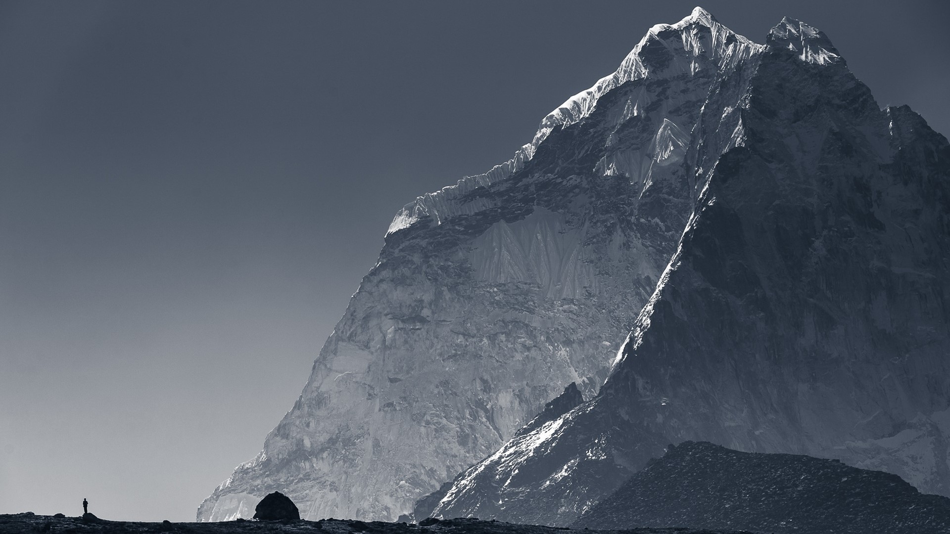 Silhouette of a person on a rocky mountain landscape with snow-capped peaks HD Wallpaper