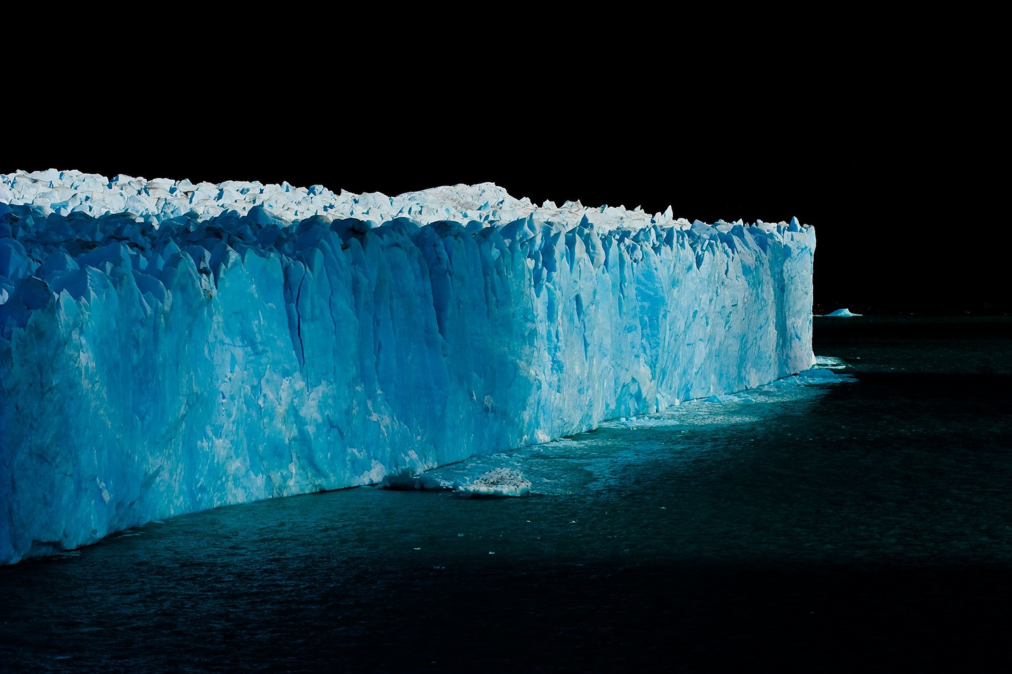 Massive blue glacier wall in dark water HD Wallpaper
