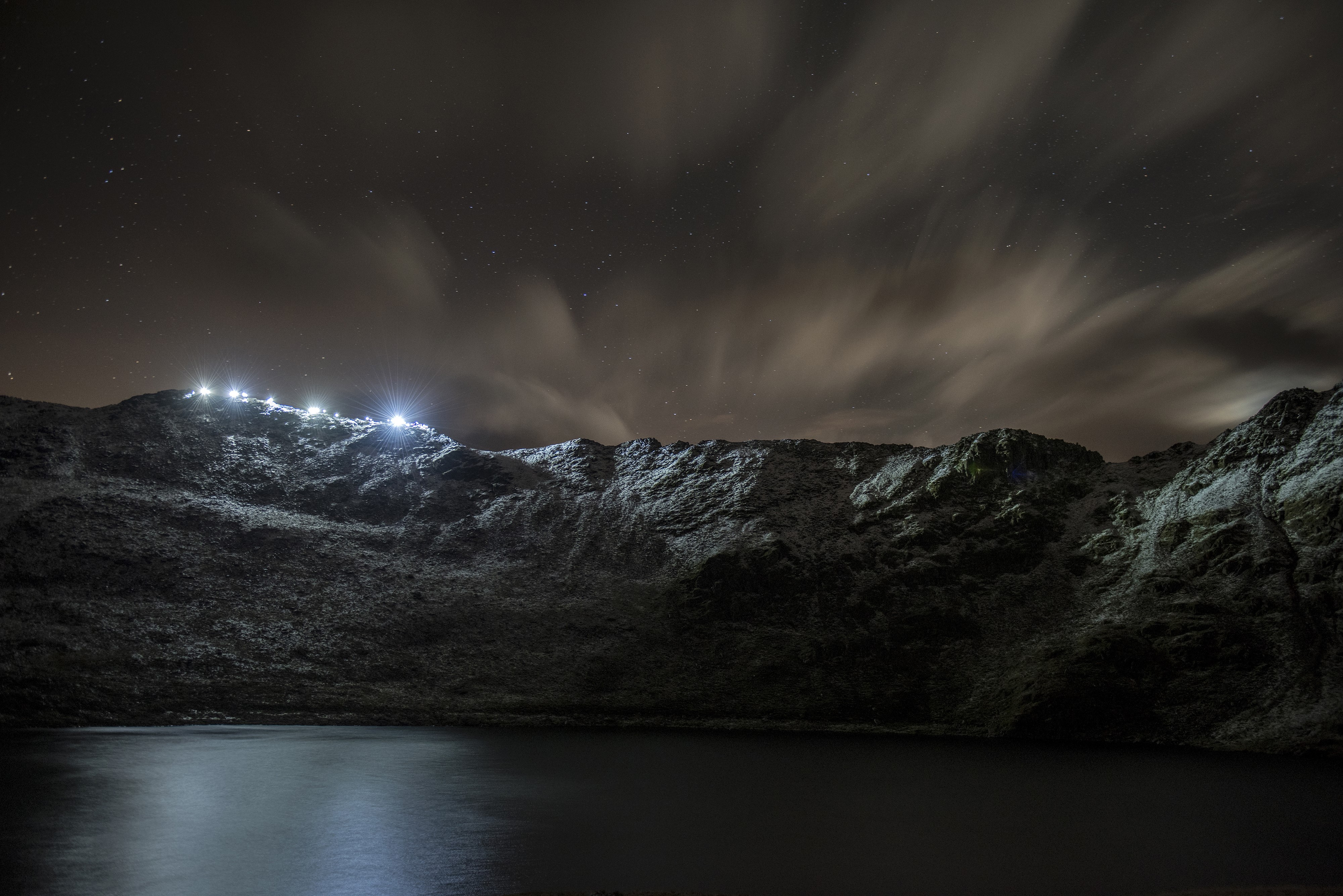 Night landscape with stars, clouds, and lights on mountains over water HD Wallpaper