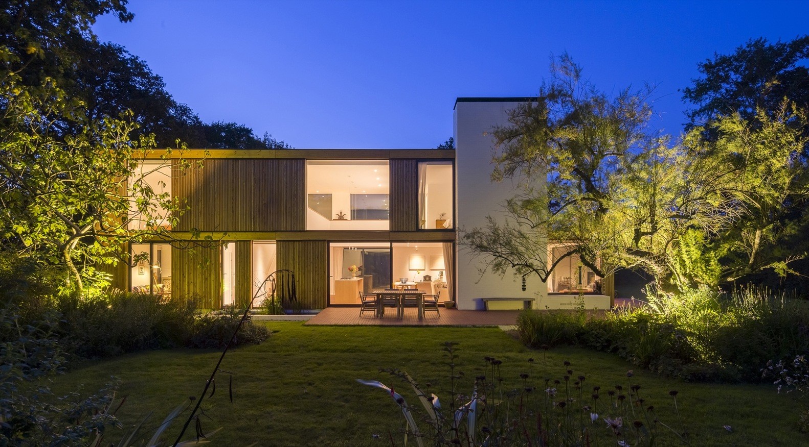 Modern wooden house at dusk with garden lighting HD Wallpaper