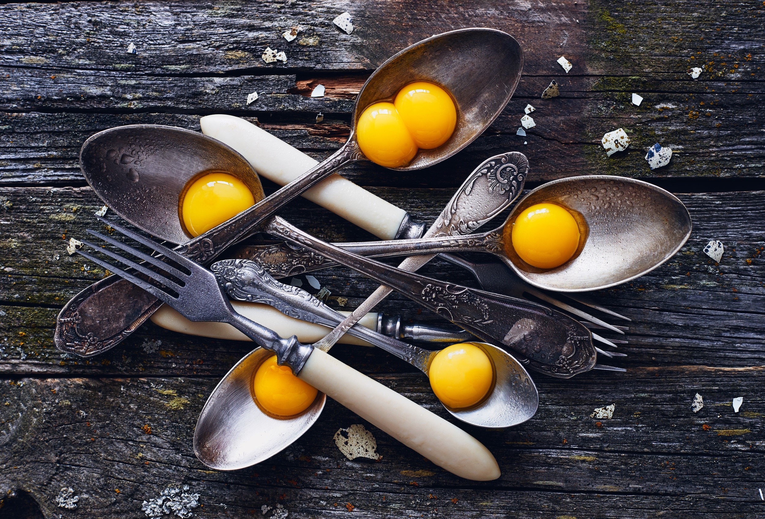 Egg yolks in antique spoons and forks on wooden table HD Wallpaper