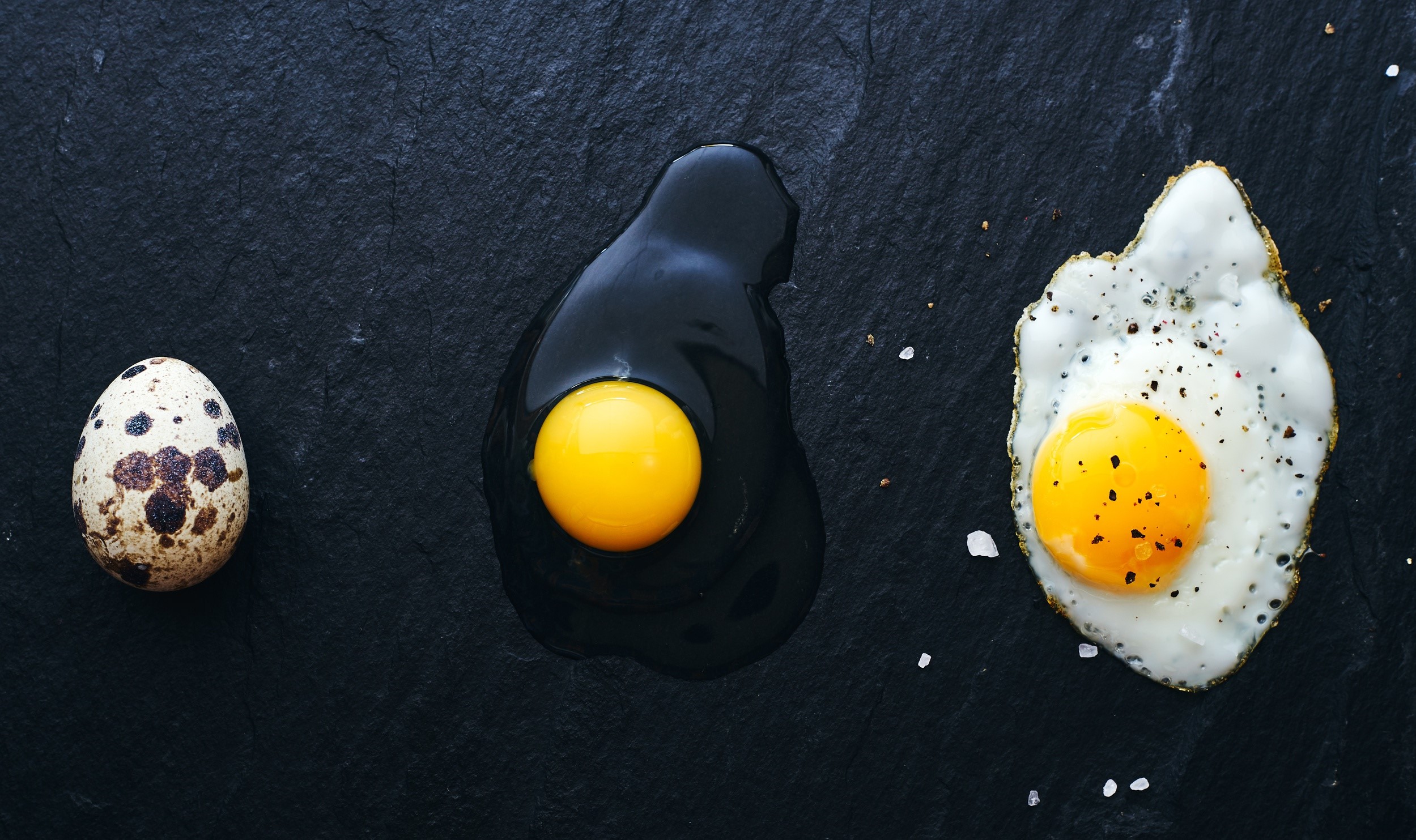 Quail egg, raw egg, and fried egg on black slate HD Wallpaper