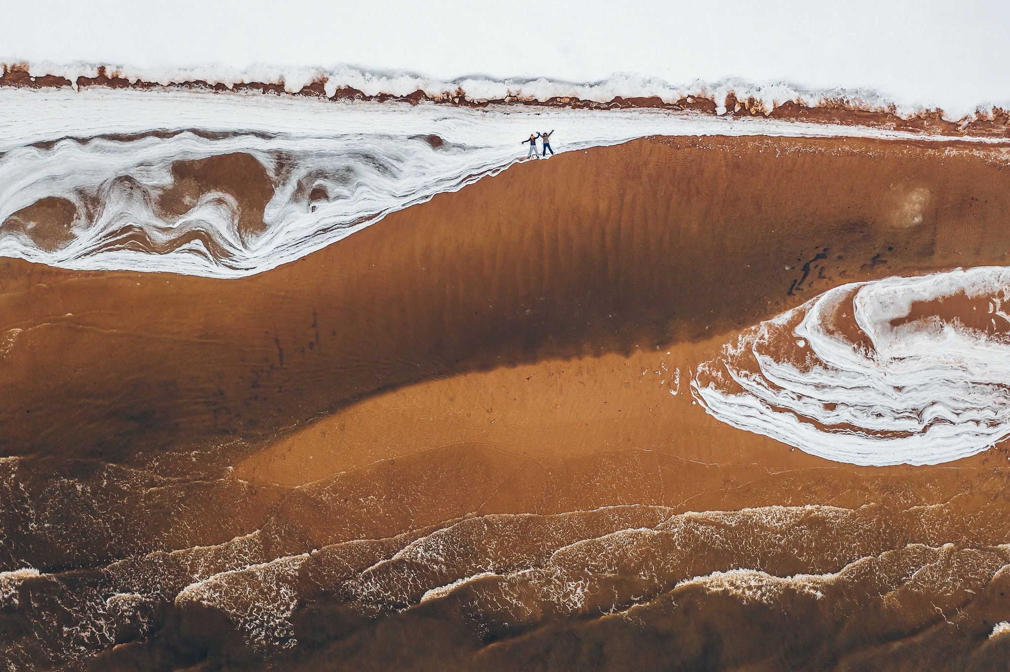 Two people on a sandy beach with waves and snow HD Wallpaper