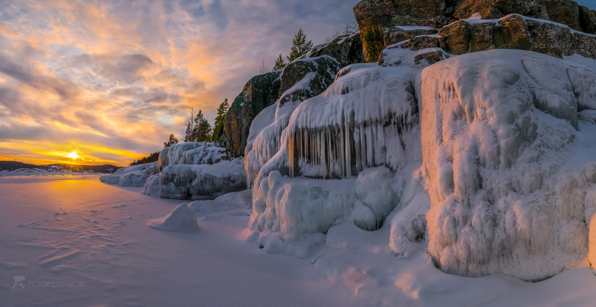 Frozen icicles on rocks by a snowy lake at sunset HD Wallpaper