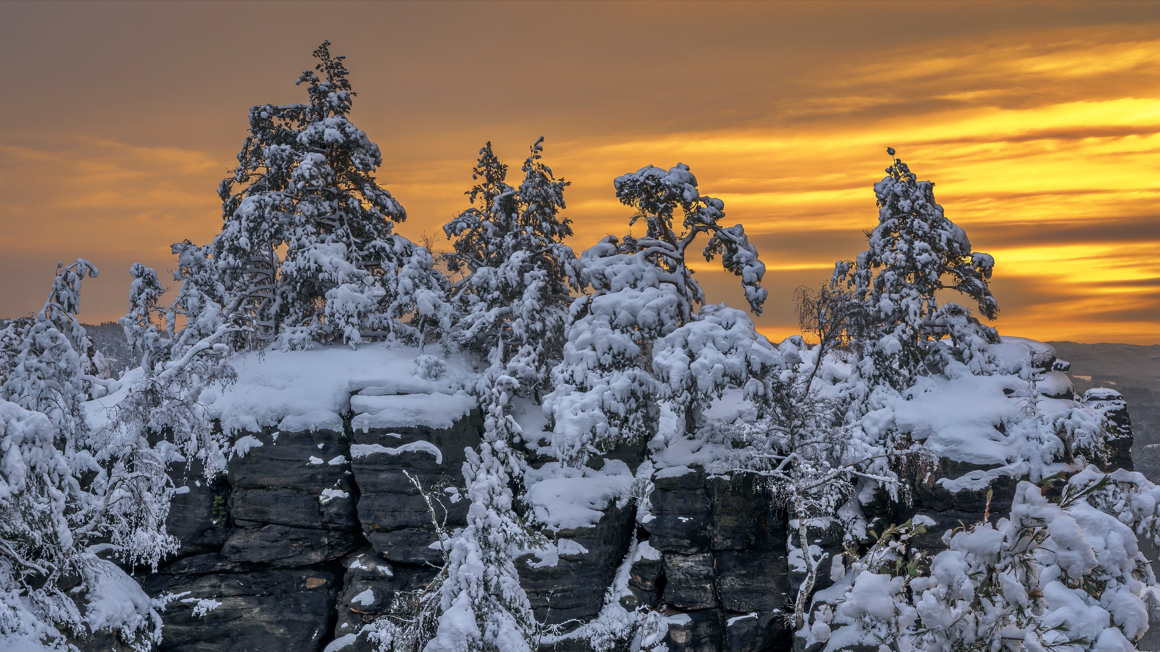 Snow-covered trees on rocky outcrops at sunset HD Wallpaper