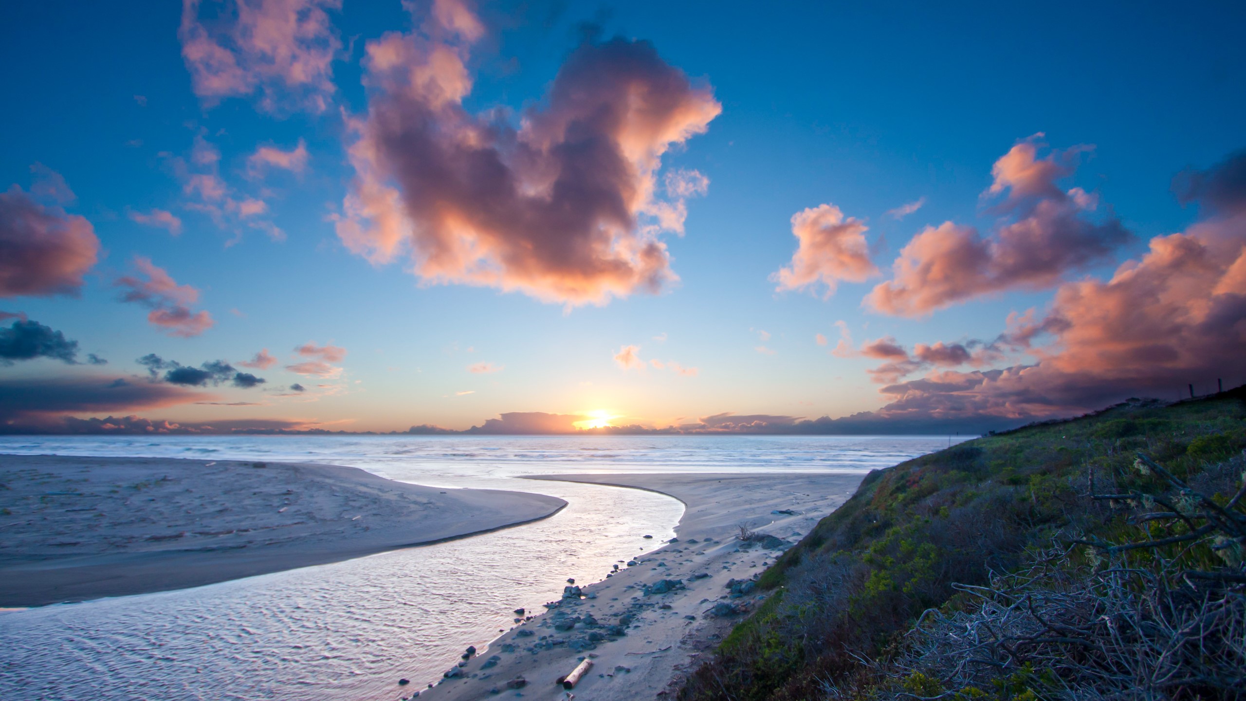 Sunset over the ocean with clouds and a river flowing to the sea HD Wallpaper