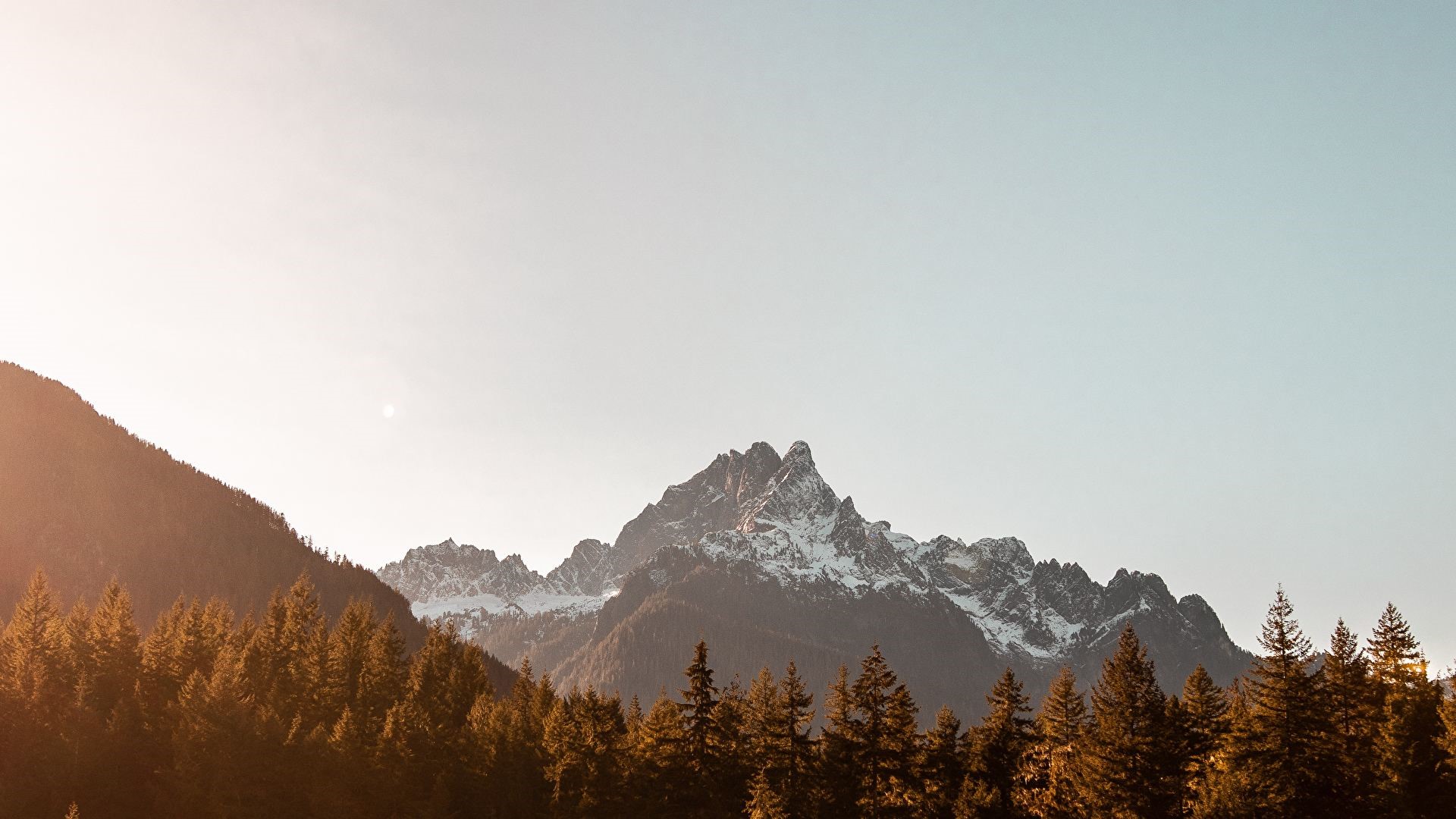 Snowy mountain range behind a forest HD Wallpaper