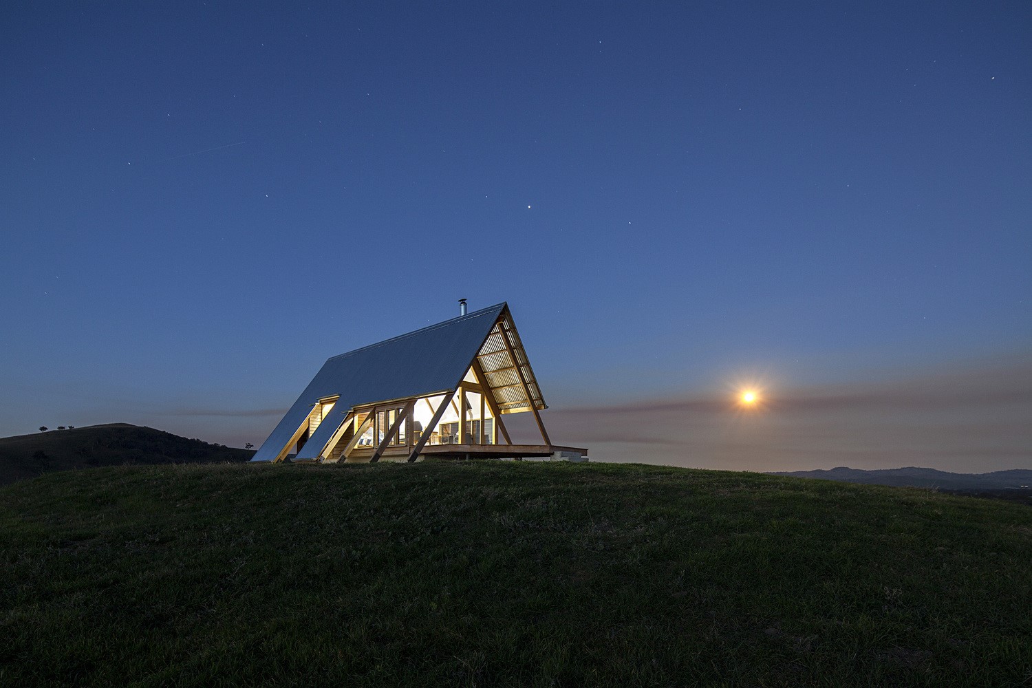 Modern A-frame house on a grassy hill at dusk HD Wallpaper