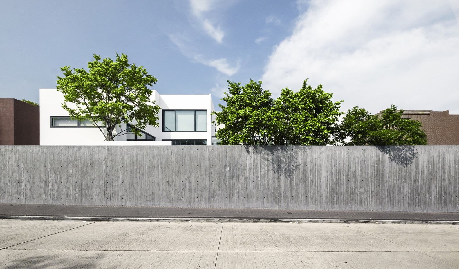 Modern white house behind a concrete wall with trees HD Wallpaper