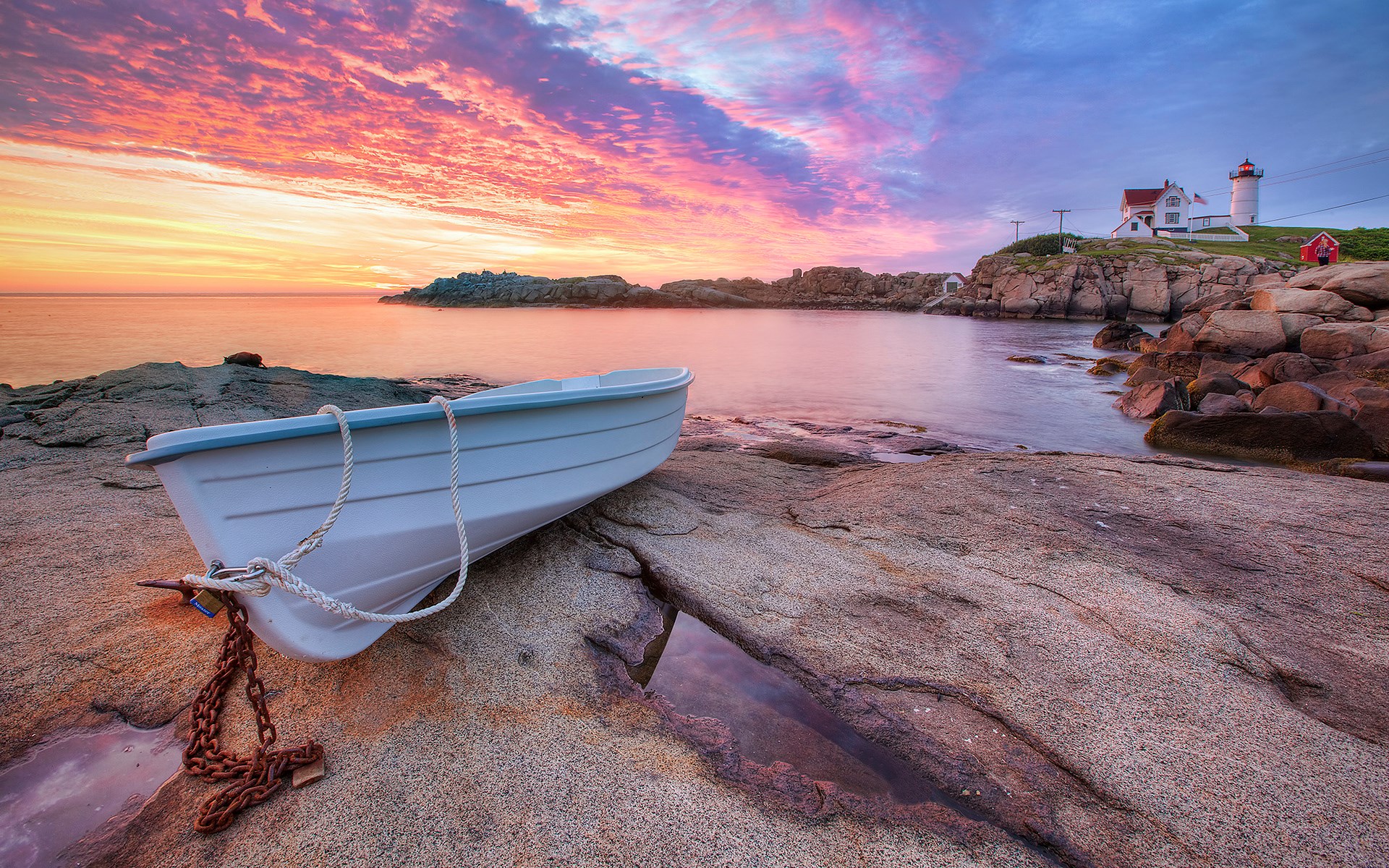 White rowboat on rocky shore with lighthouse at sunset HD Wallpaper