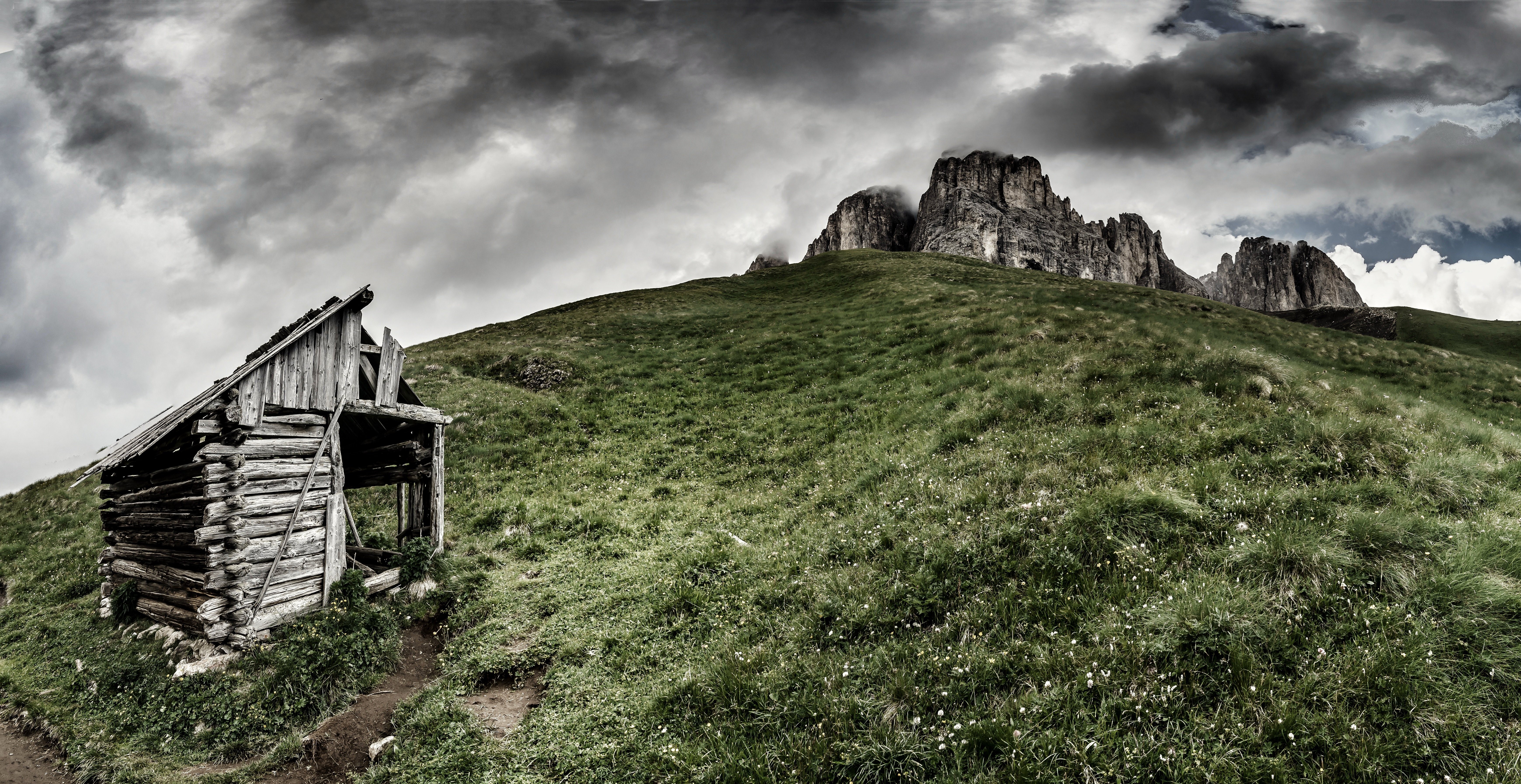 Abandoned wooden cabin on a grassy mountain slope under dark clouds HD Wallpaper