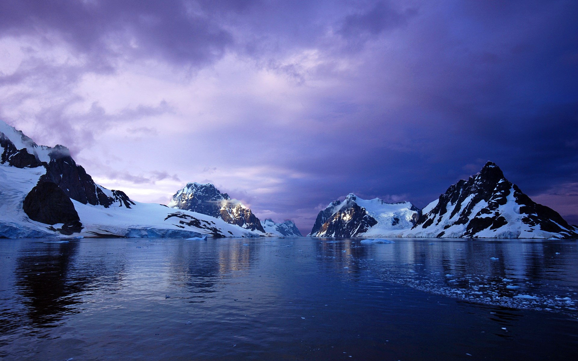 Snow-capped mountains reflected in calm water under a purple sky HD Wallpaper