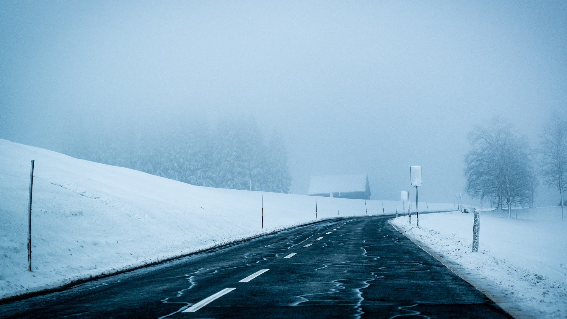 Winding road through a snowy, misty winter landscape HD Wallpaper