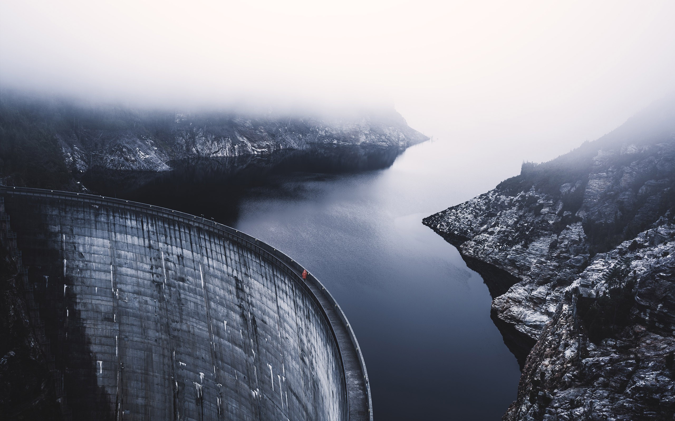 Curved concrete dam in misty mountains with dark water HD Wallpaper
