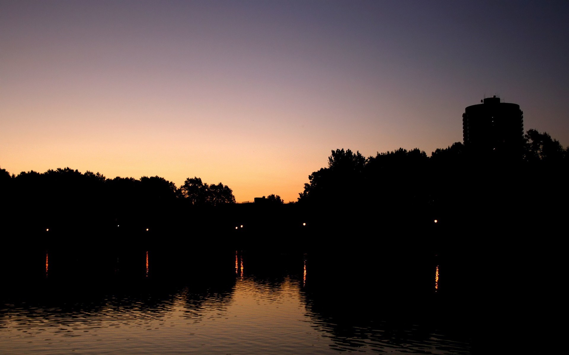 Silhouette of trees and a tower by a lake at dusk HD Wallpaper