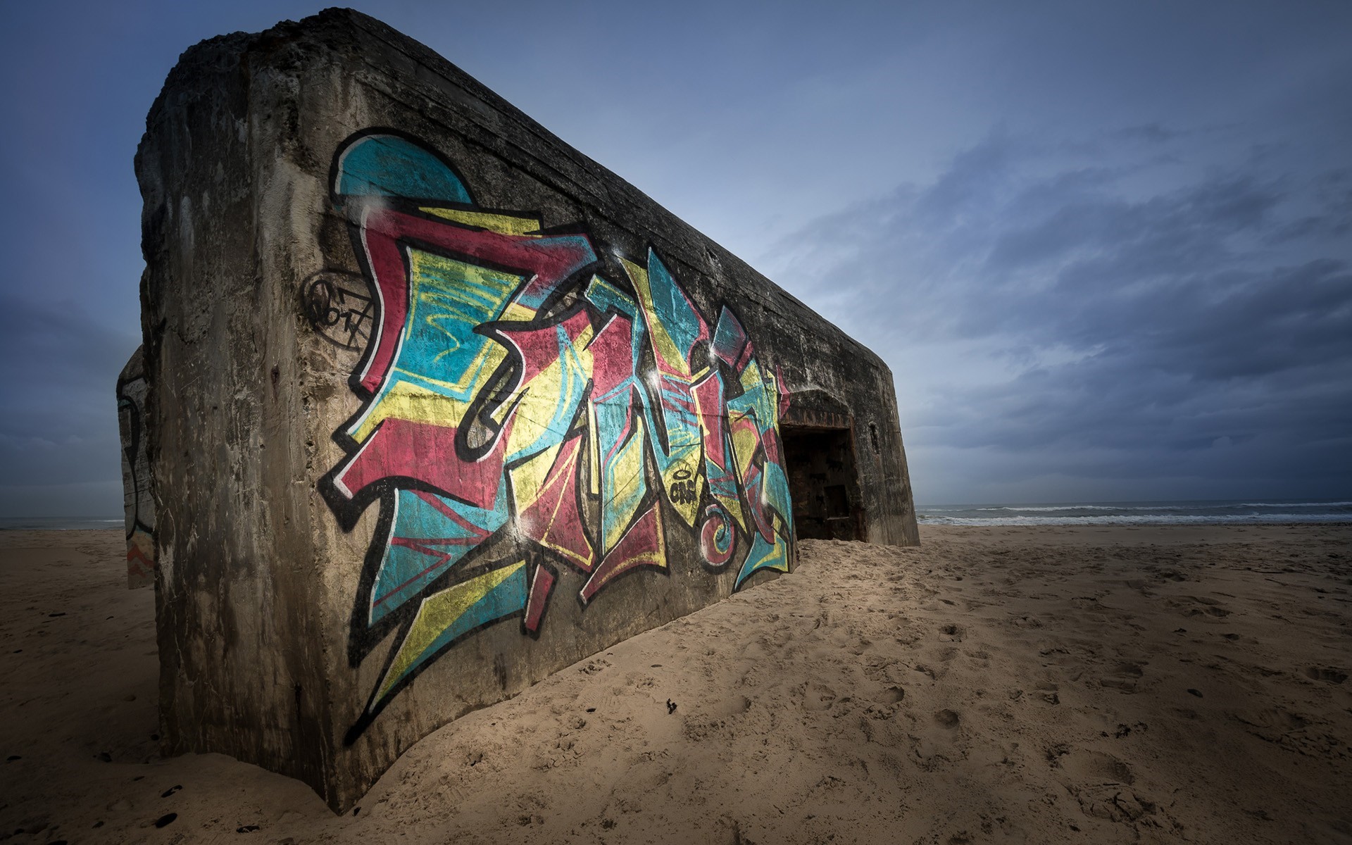 Graffiti covered concrete bunker on a sandy beach HD Wallpaper