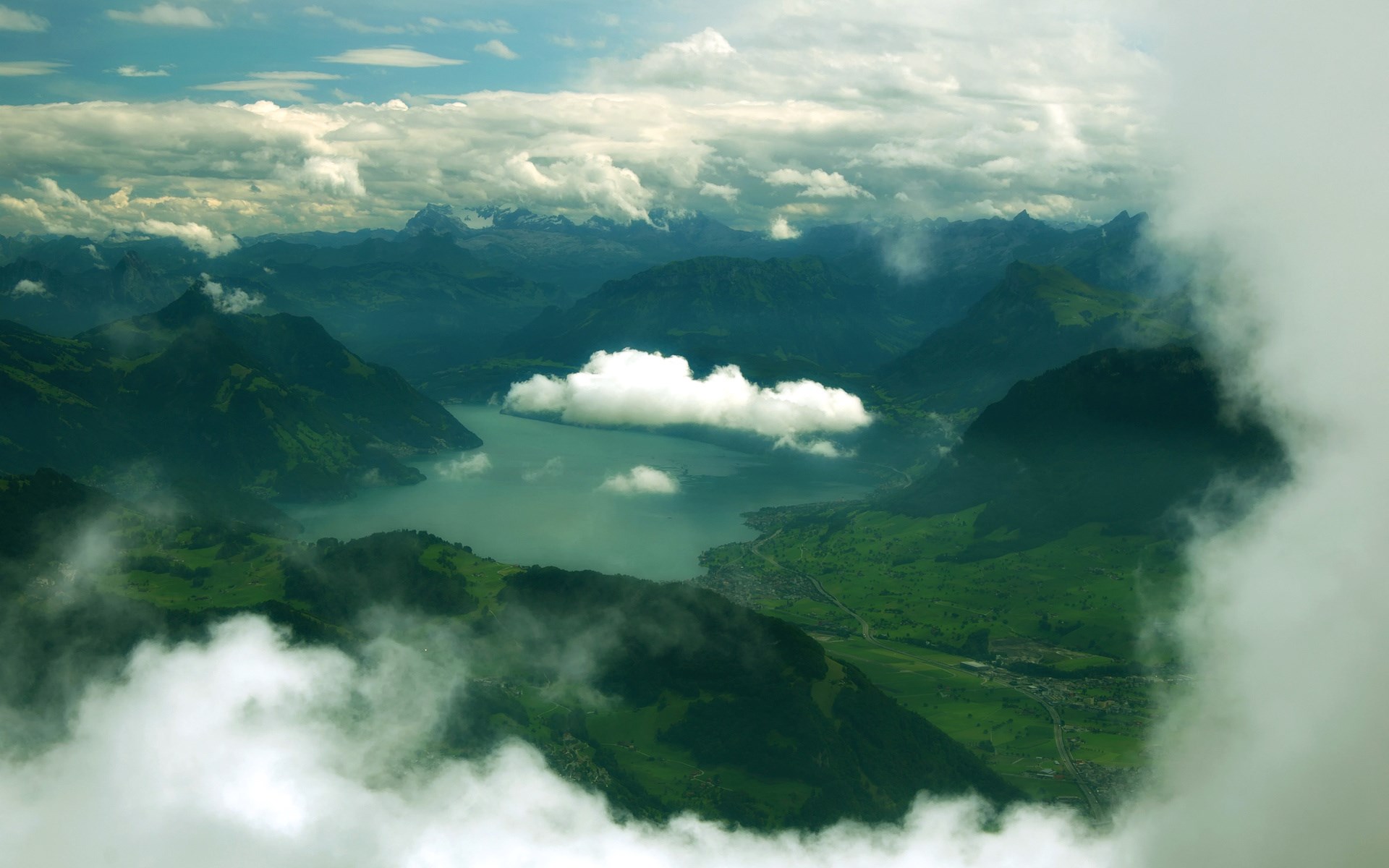Aerial view of a lake surrounded by green mountains and clouds HD Wallpaper