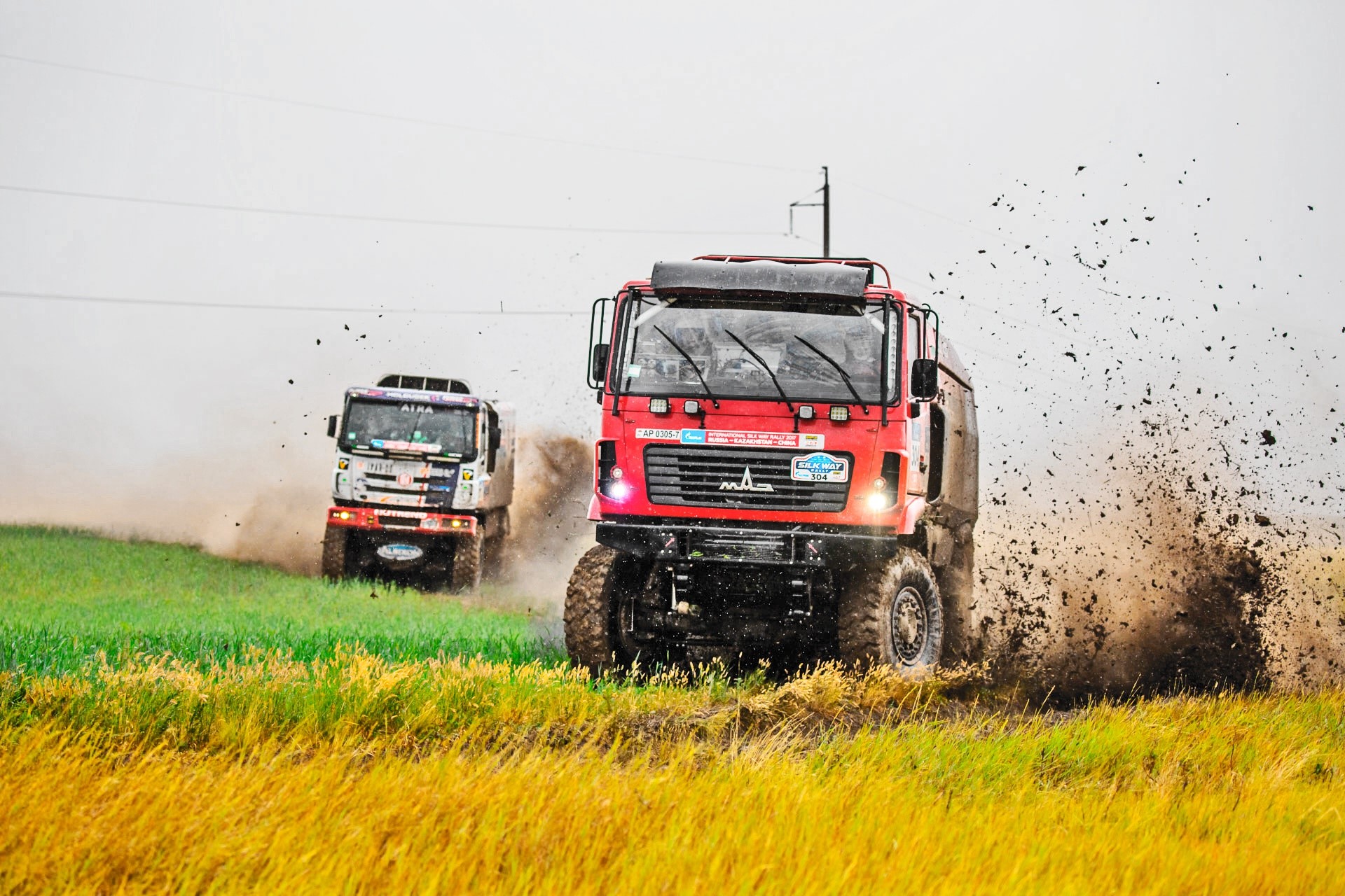Two rally trucks racing through mud and grass HD Wallpaper