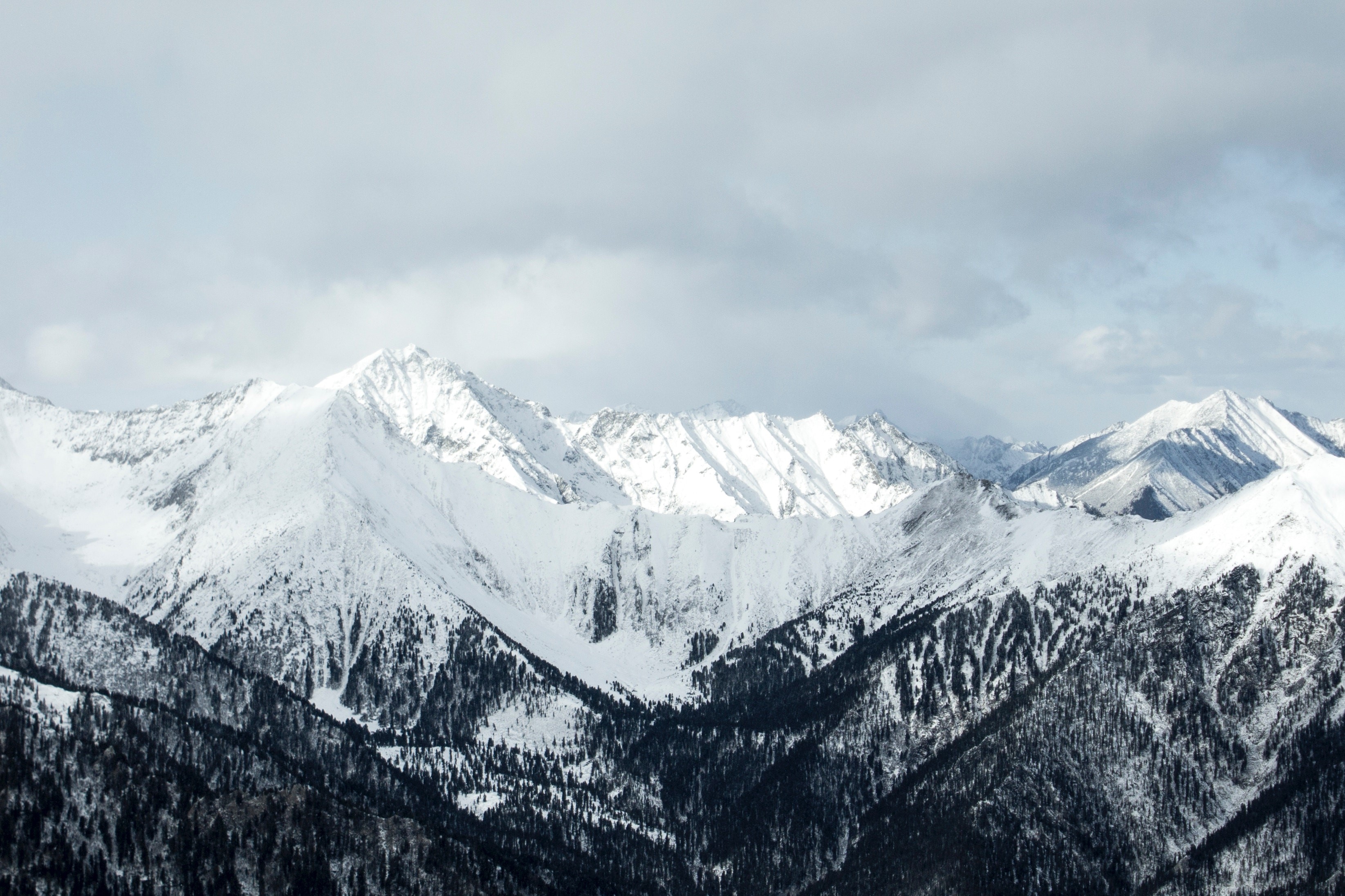 Snow-covered mountains under a cloudy sky HD Wallpaper