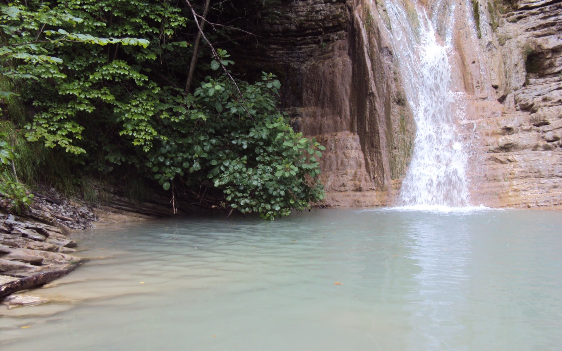 Waterfall cascading into a clear pool surrounded by rocks and trees HD Wallpaper
