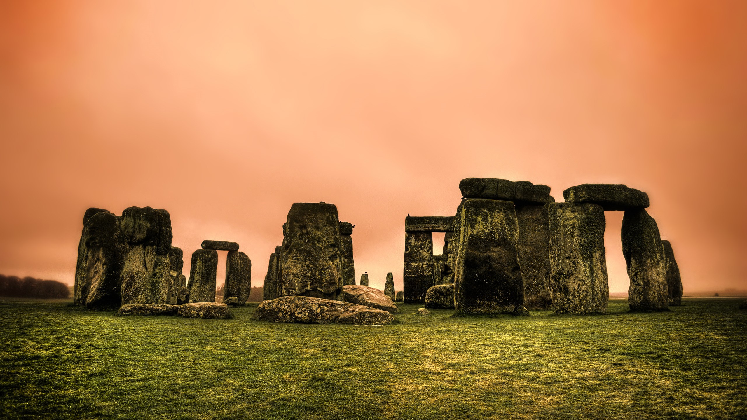 Stonehenge ancient monument on grassy field under orange sky HD Wallpaper