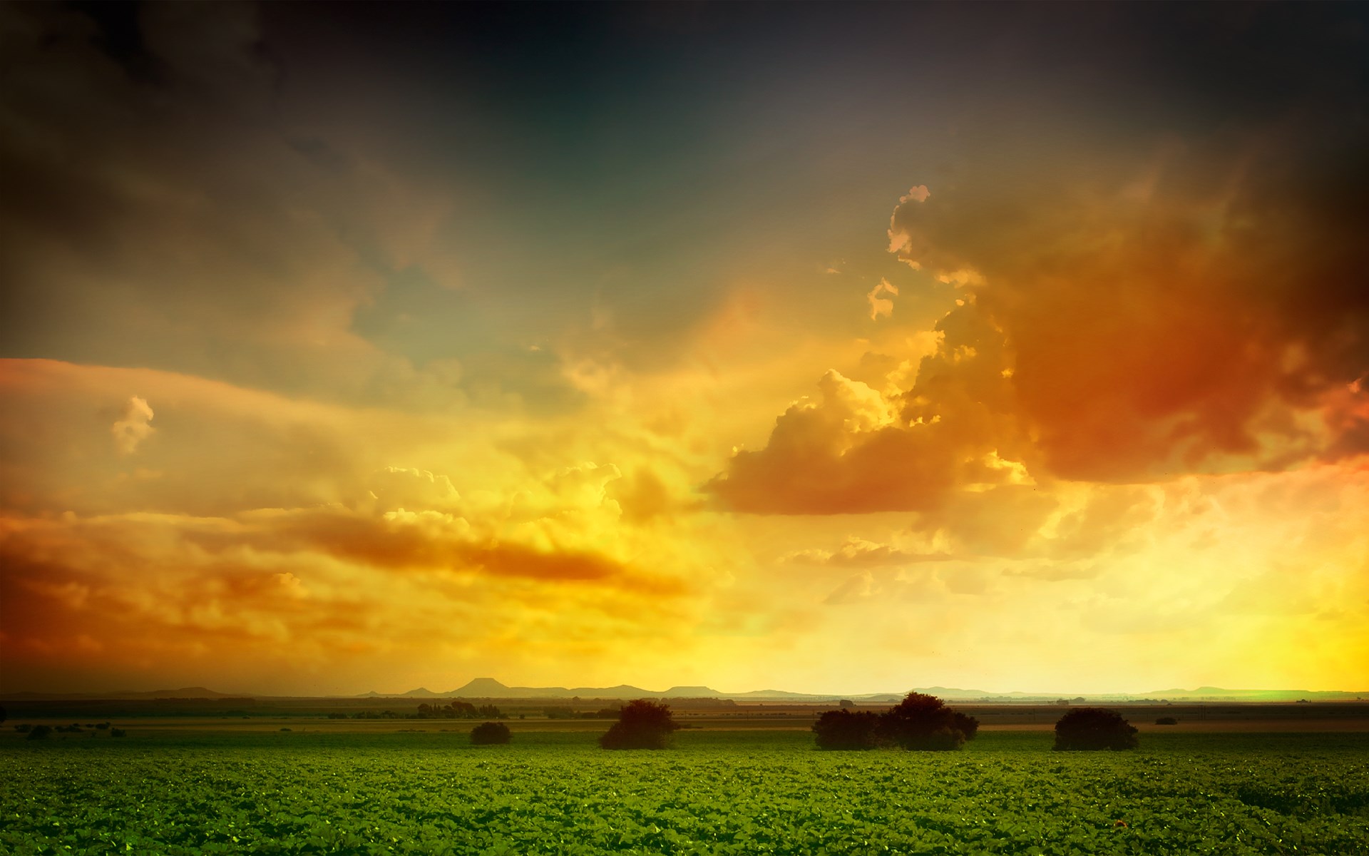 Dramatic sunset over a green field with distant hills HD Wallpaper